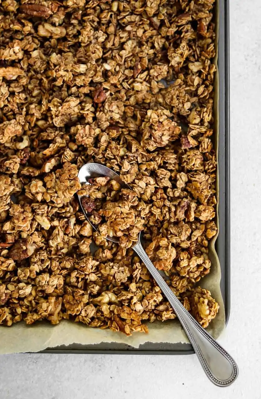 Baked granola on a baking tray with a spoon. 