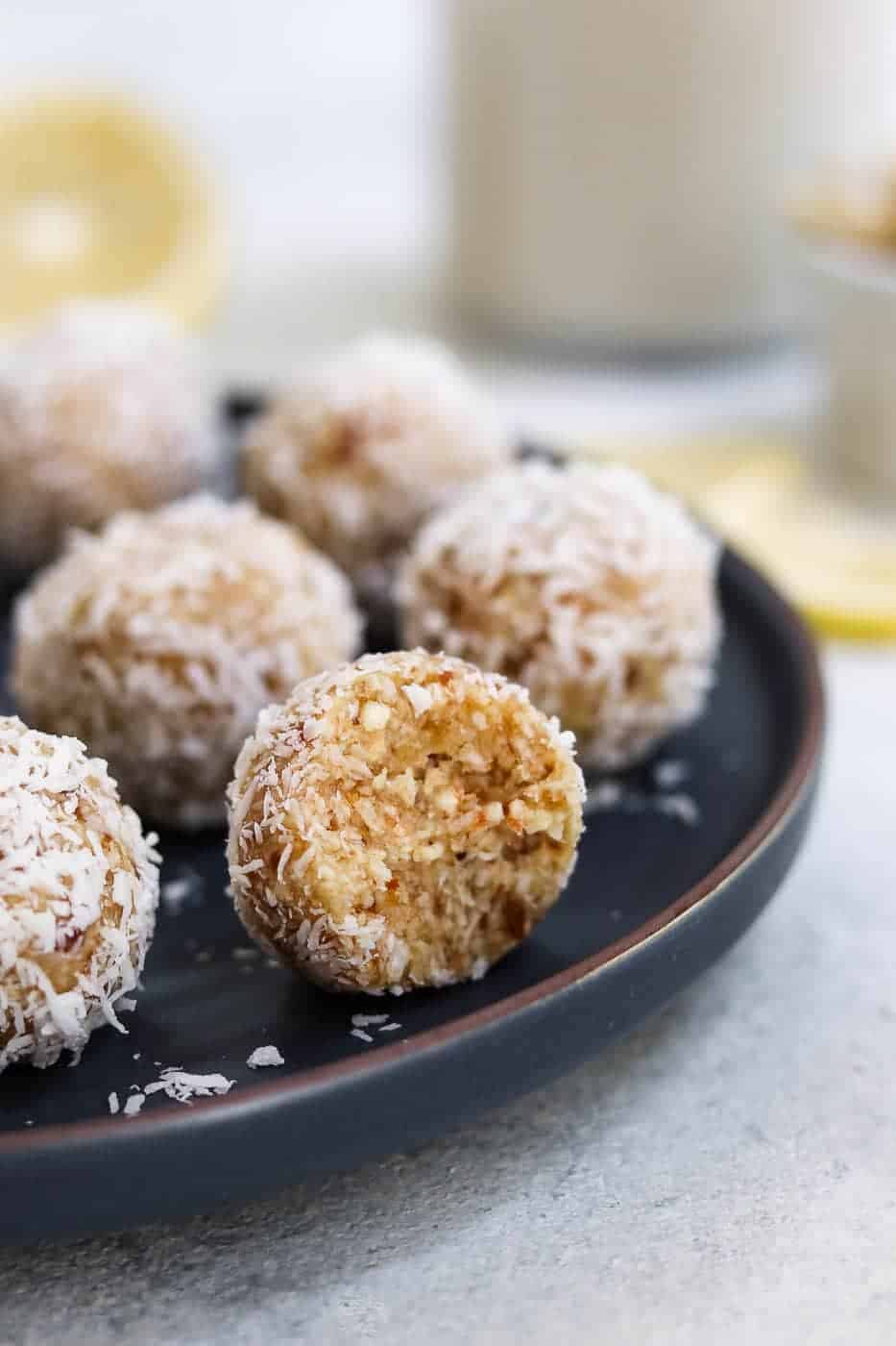 Lemon coconut energy balls on a dark blue plate with one bite taken out. 