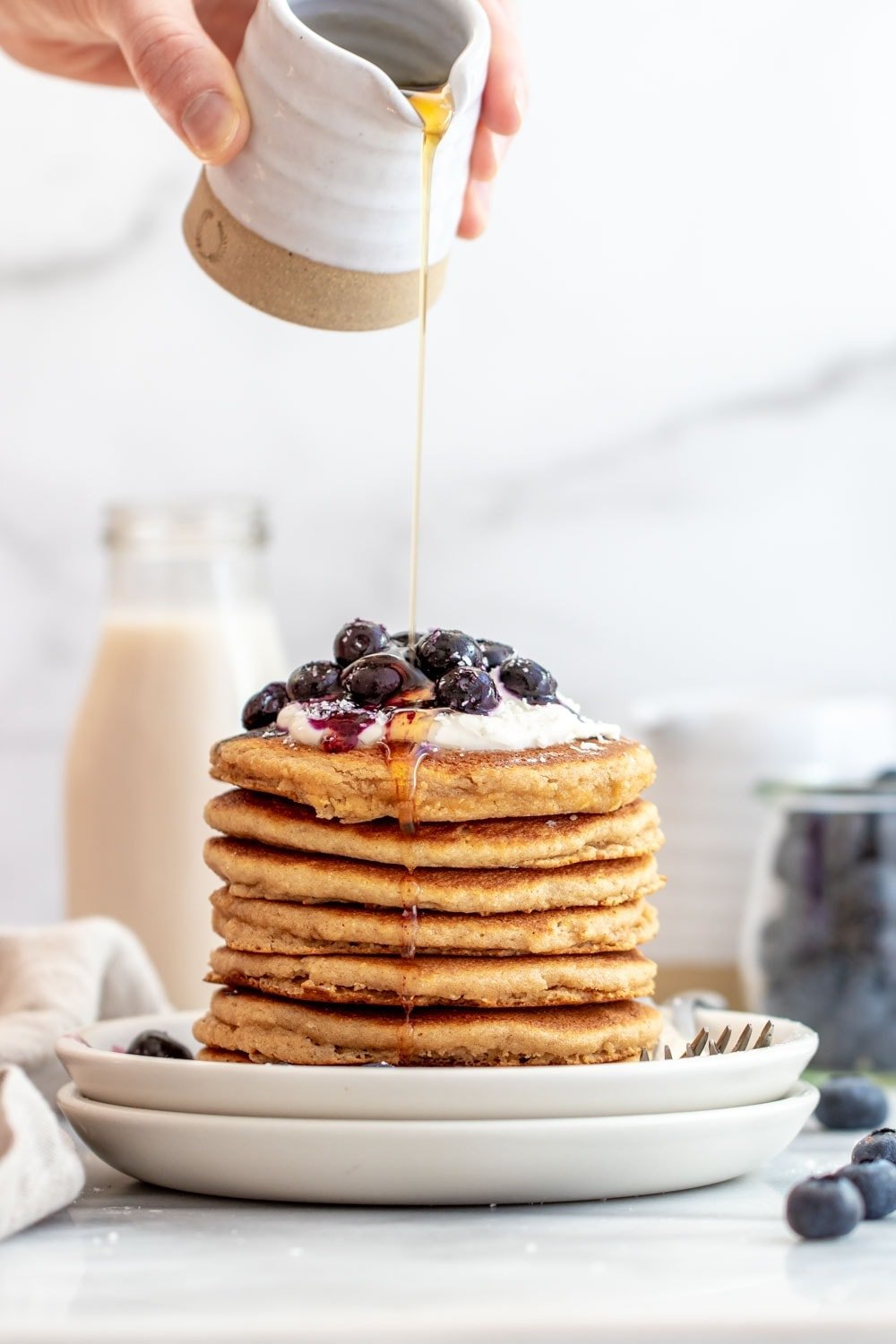 pouring maple syrup on a tall stack of gluten free pancakes.