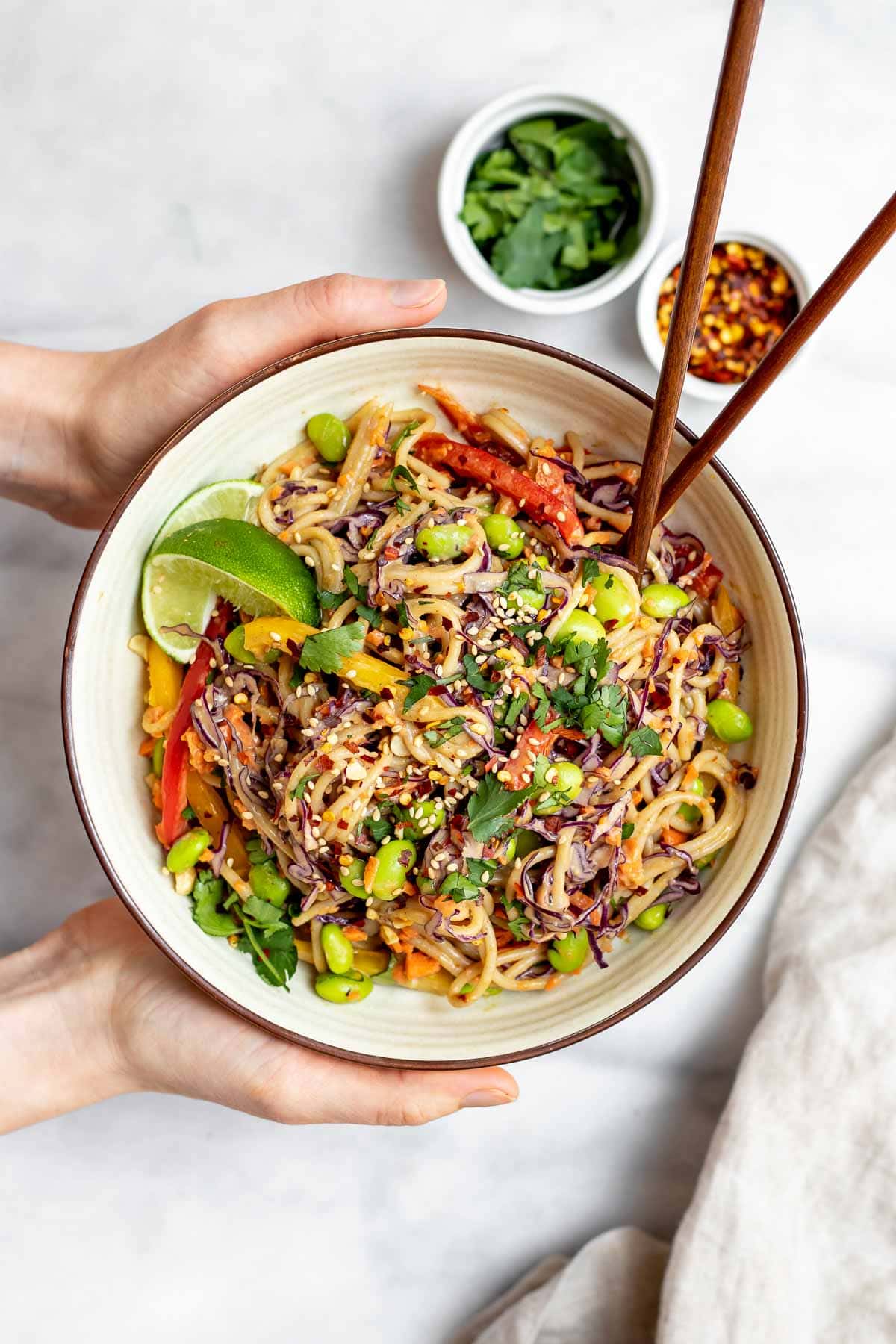 Two hands holding the thai noodle salad with chopsticks on the side.