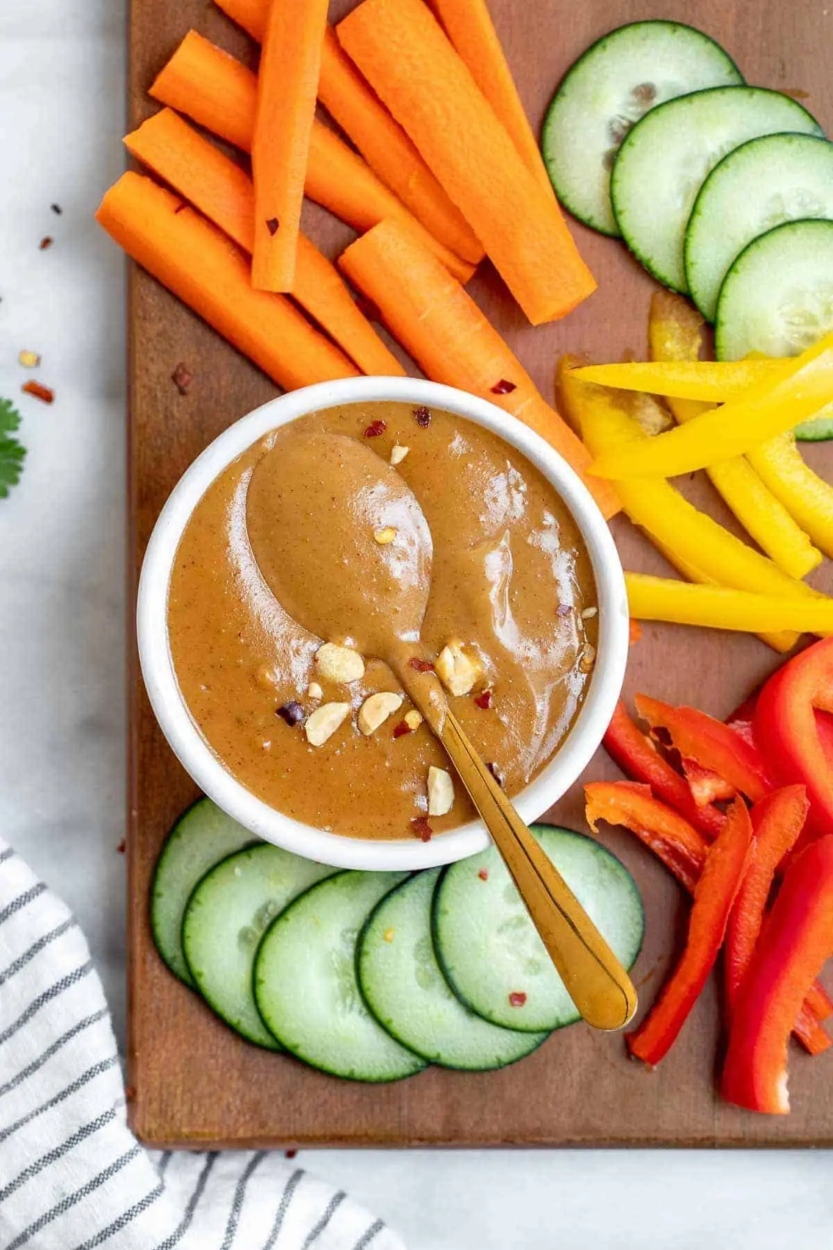 vegan Thai Peanut sauce in a white bowl with chopped vegetables arranged around it.