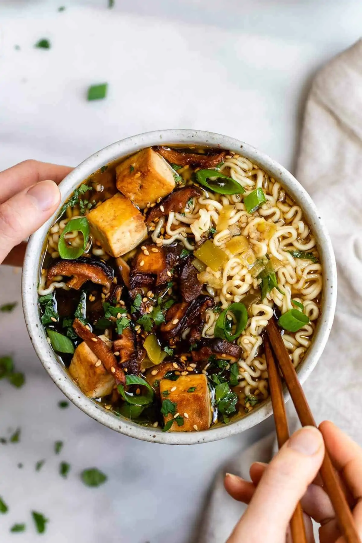 Two hands holding a bowl of vegan ramen noodles with mushrooms.