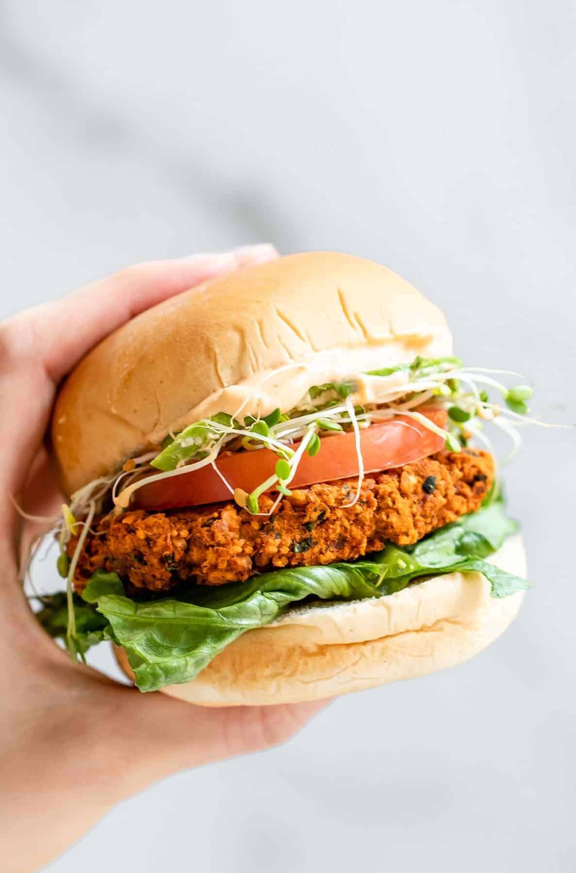 Hand holding up a chickpea burger with lettuce and tomato.