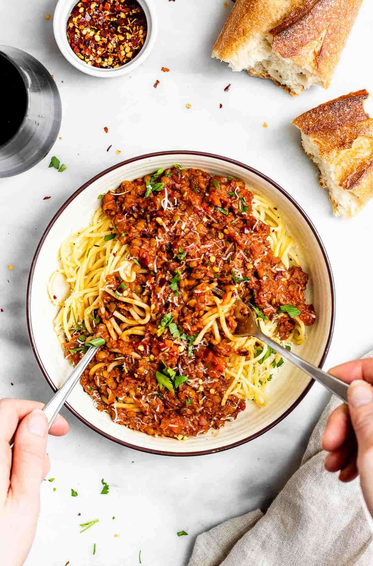 Two hands twirling together the spaghetti with lentil bolognese on top.