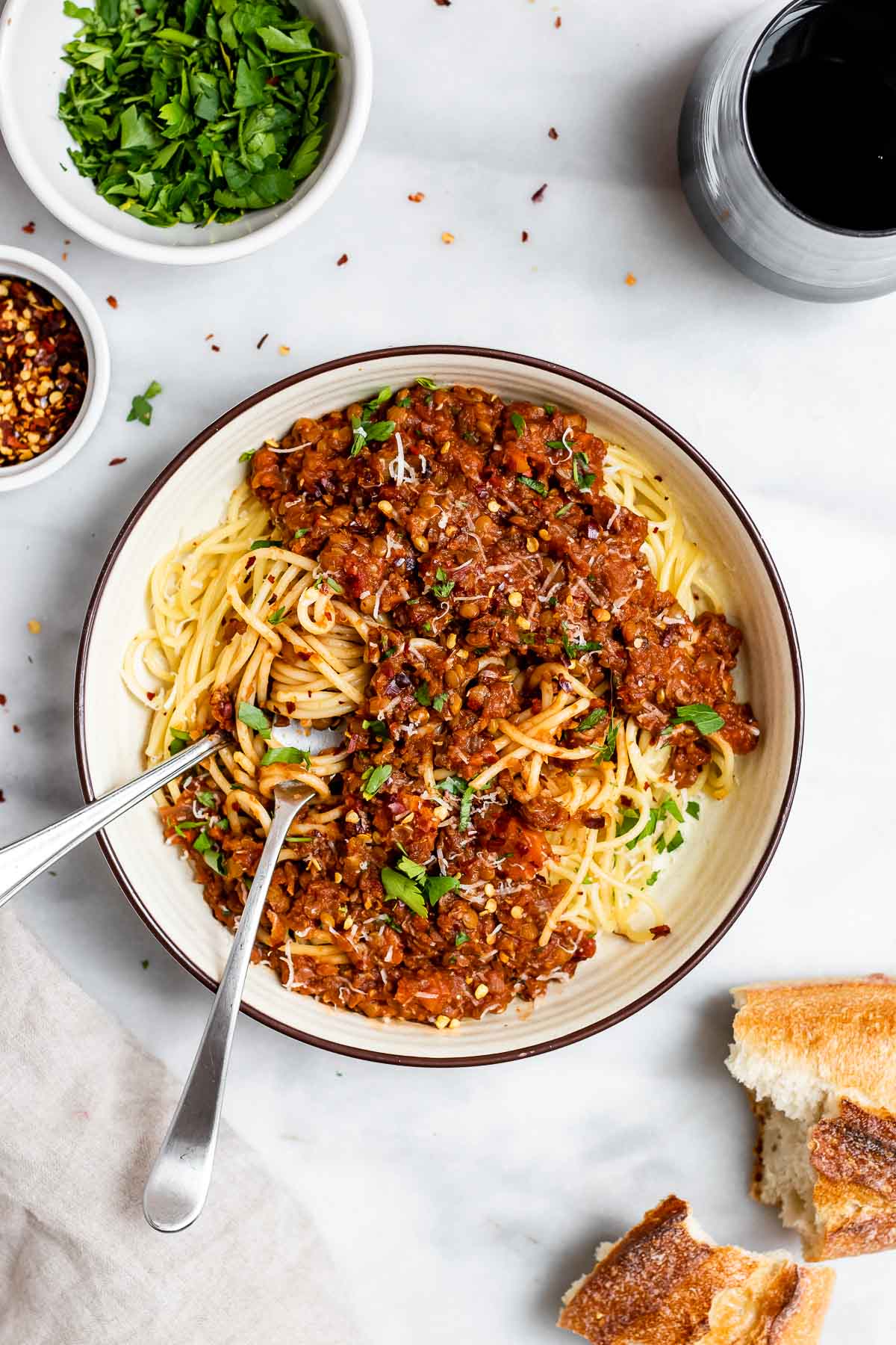 Vegan lentil bolognese in a white bowl with wine and bread on the side.