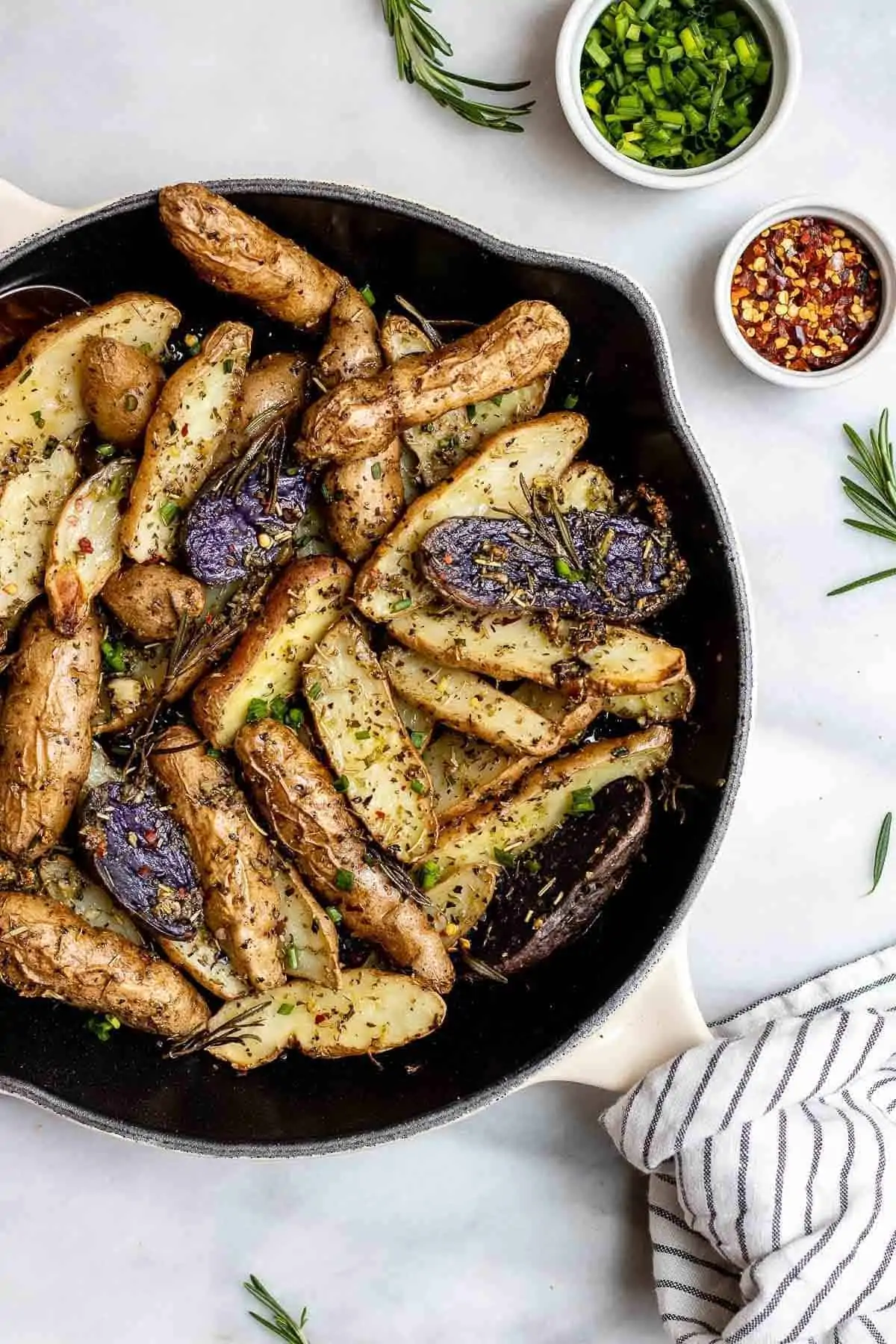 Roasted fingerling potatoes in a cast iron skillet with a towel on the handle.