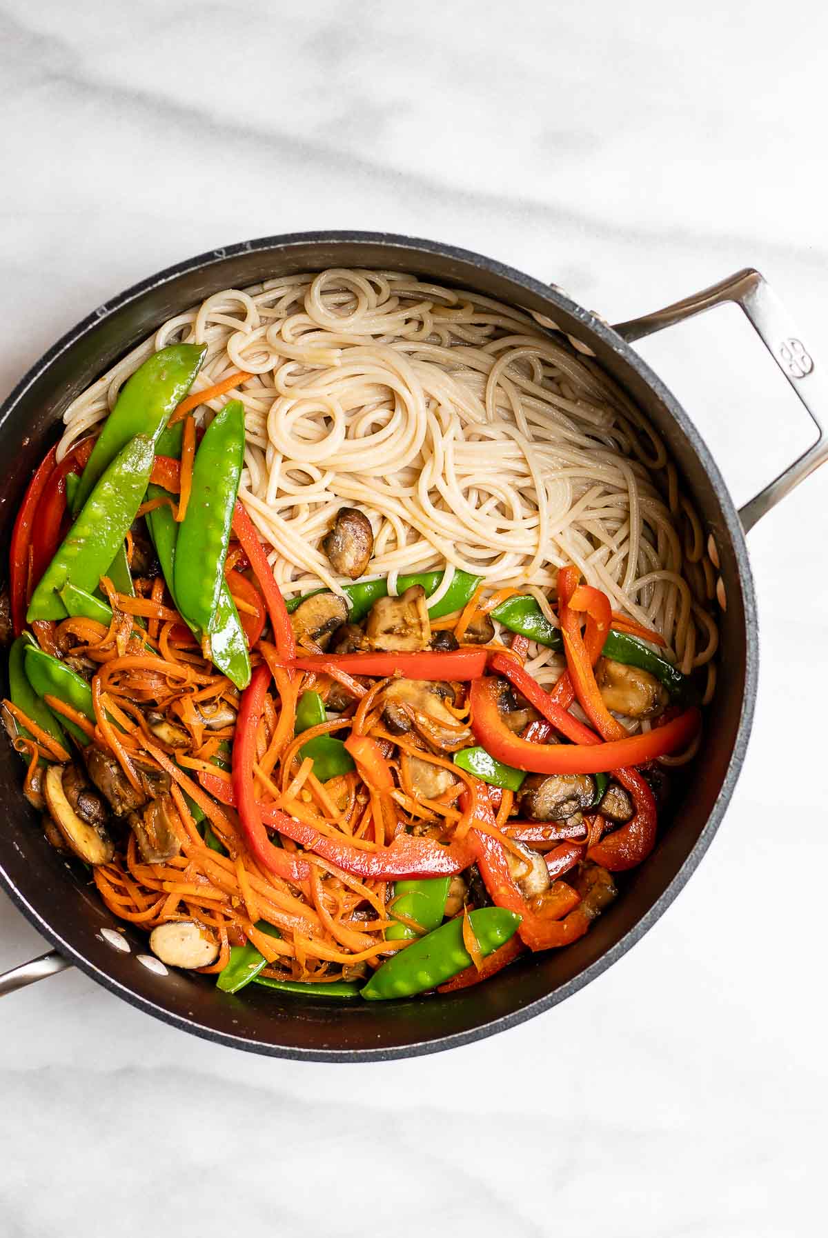 Cooked noodles and vegetables in a pot before getting mixed together.