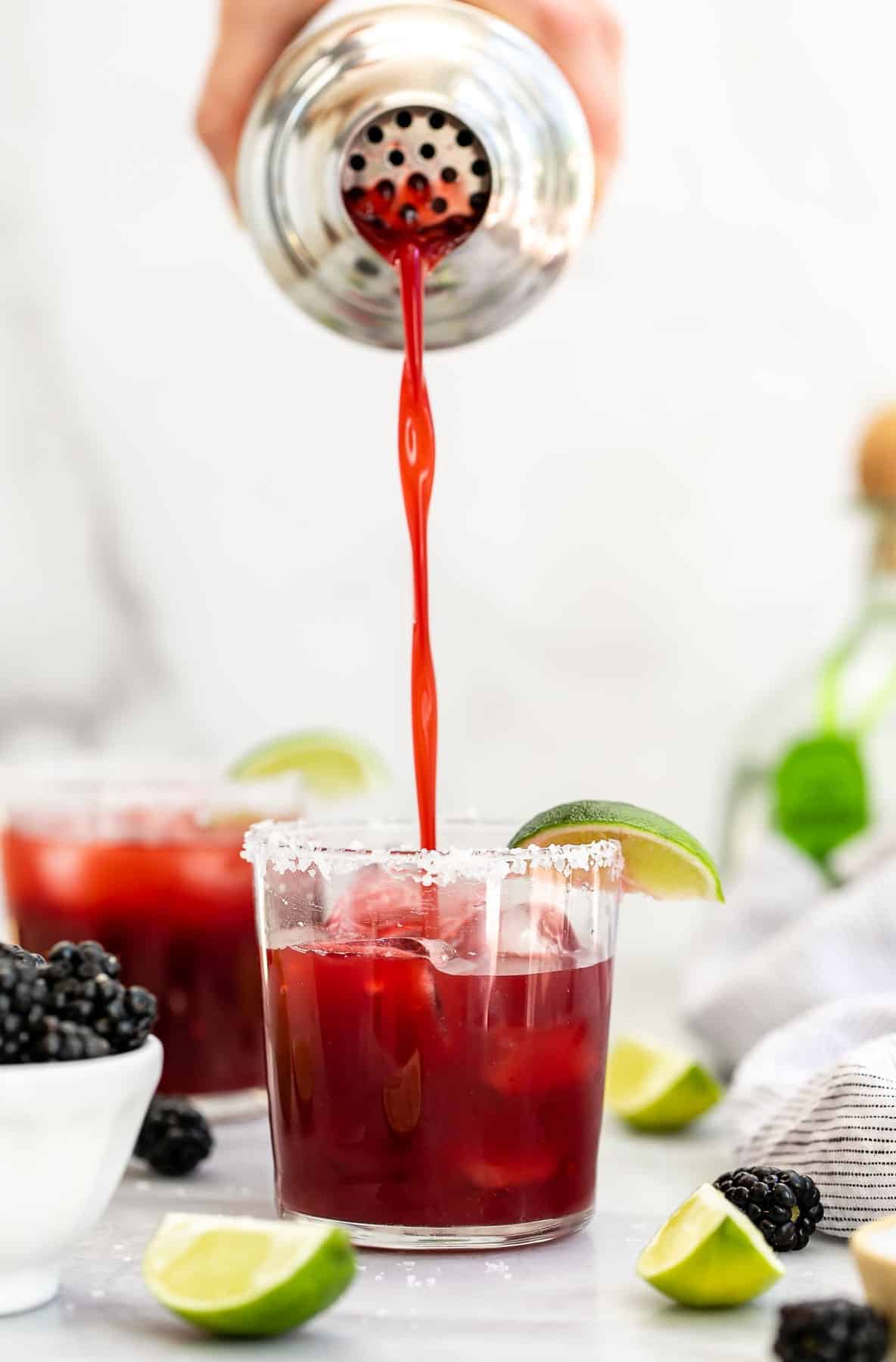 Pouring the blackberry margarita over ice in a glass.