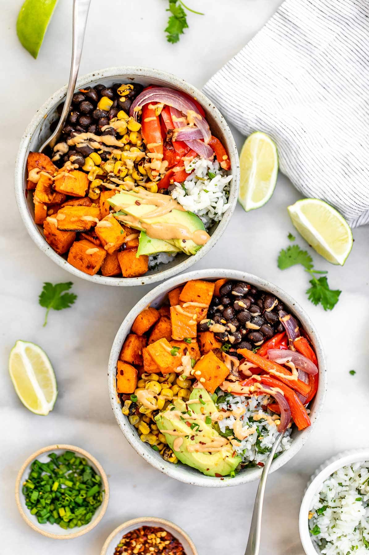 Two burrito bowls with veggies, avocado and lime on top.