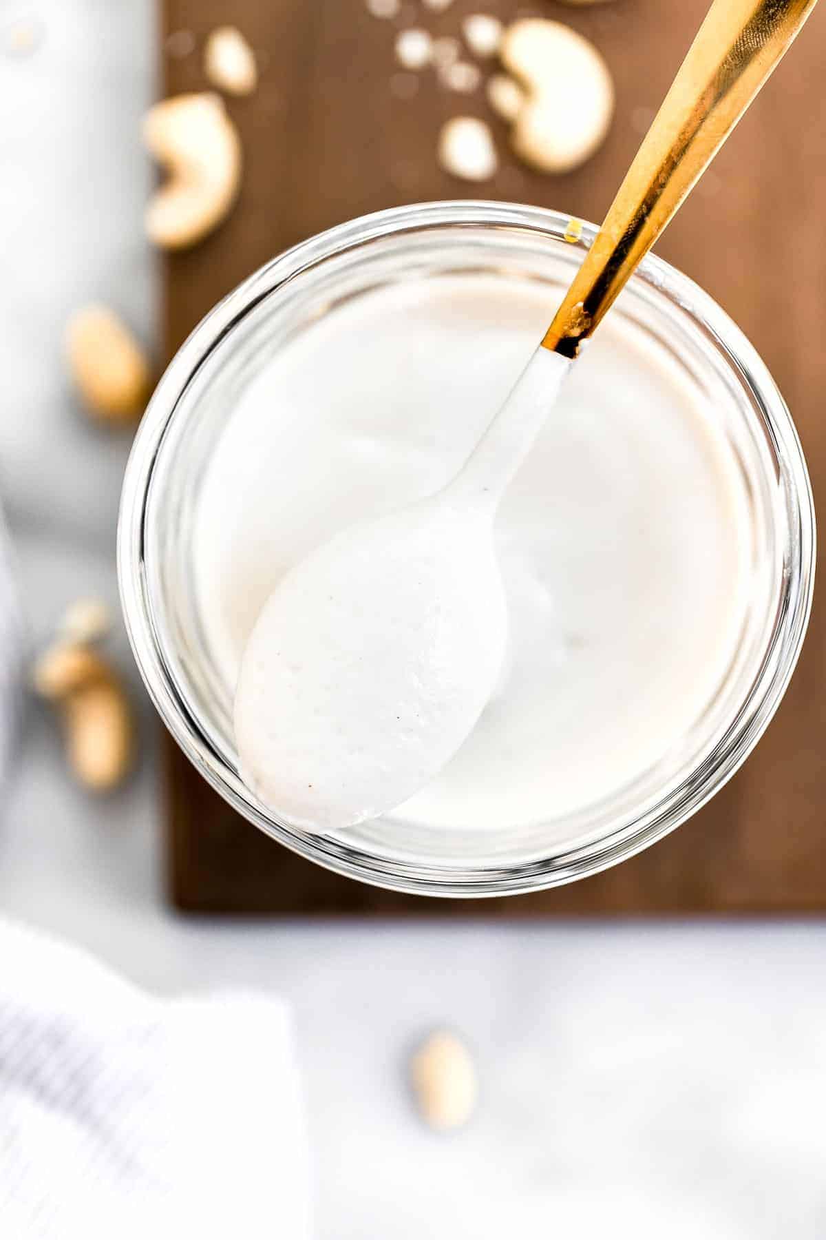 Cashew cream in a jar with a gold spoon sitting on top.
