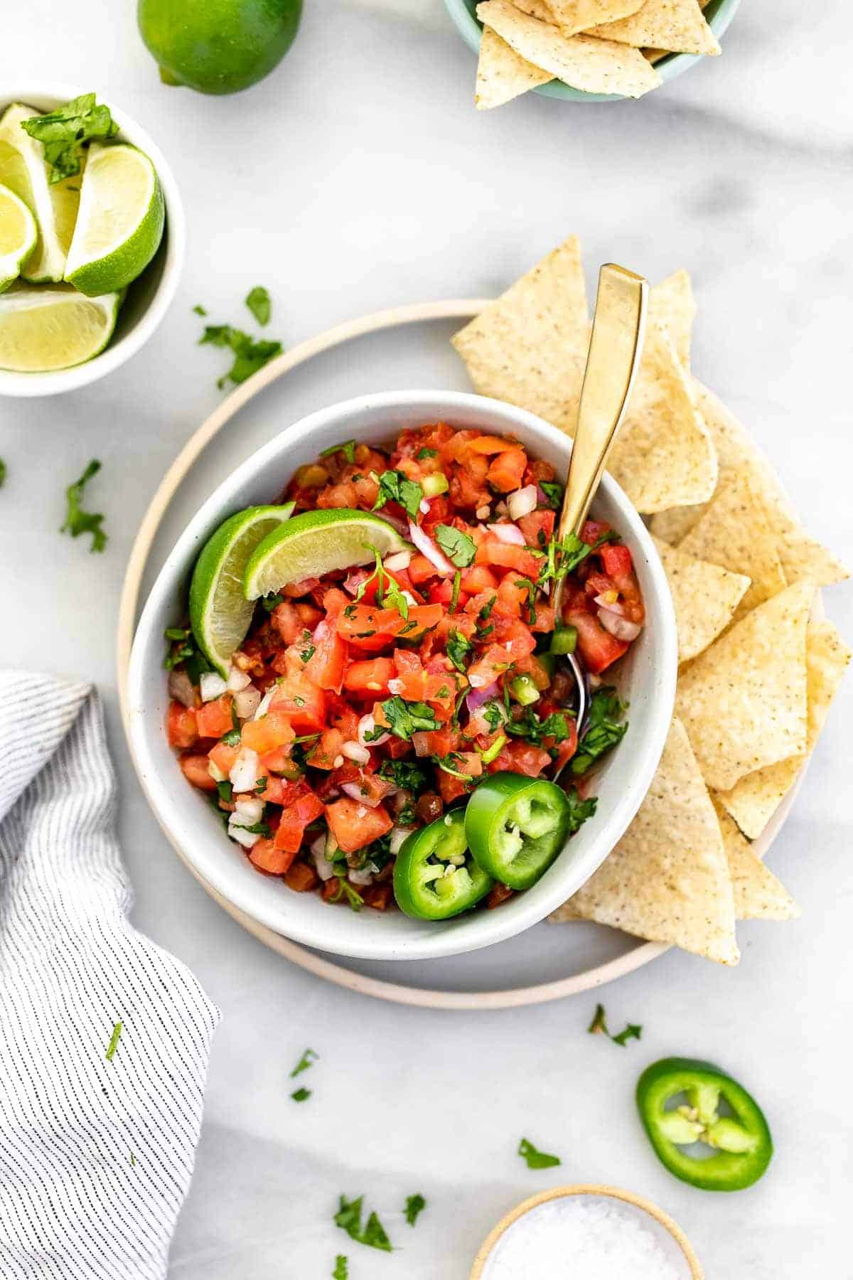 Pico de gallo in a bowl with chips and lime on the sides.