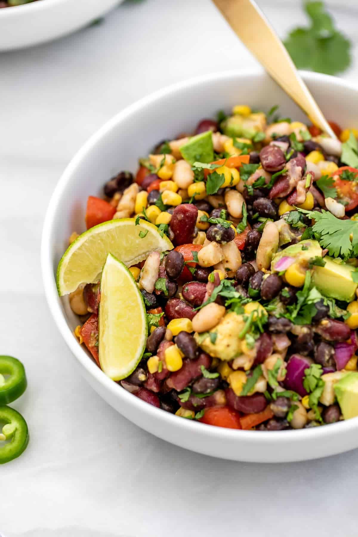 Mexican bean salad in a white bowl with lime wedges on the side.