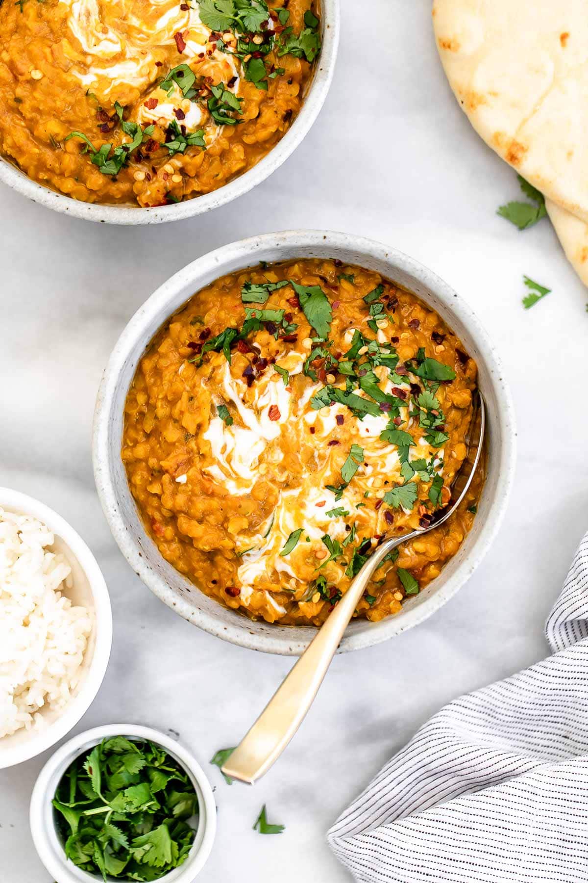 One bowl of lentil curry with yogurt and cilantro on top with a spoon on the side.