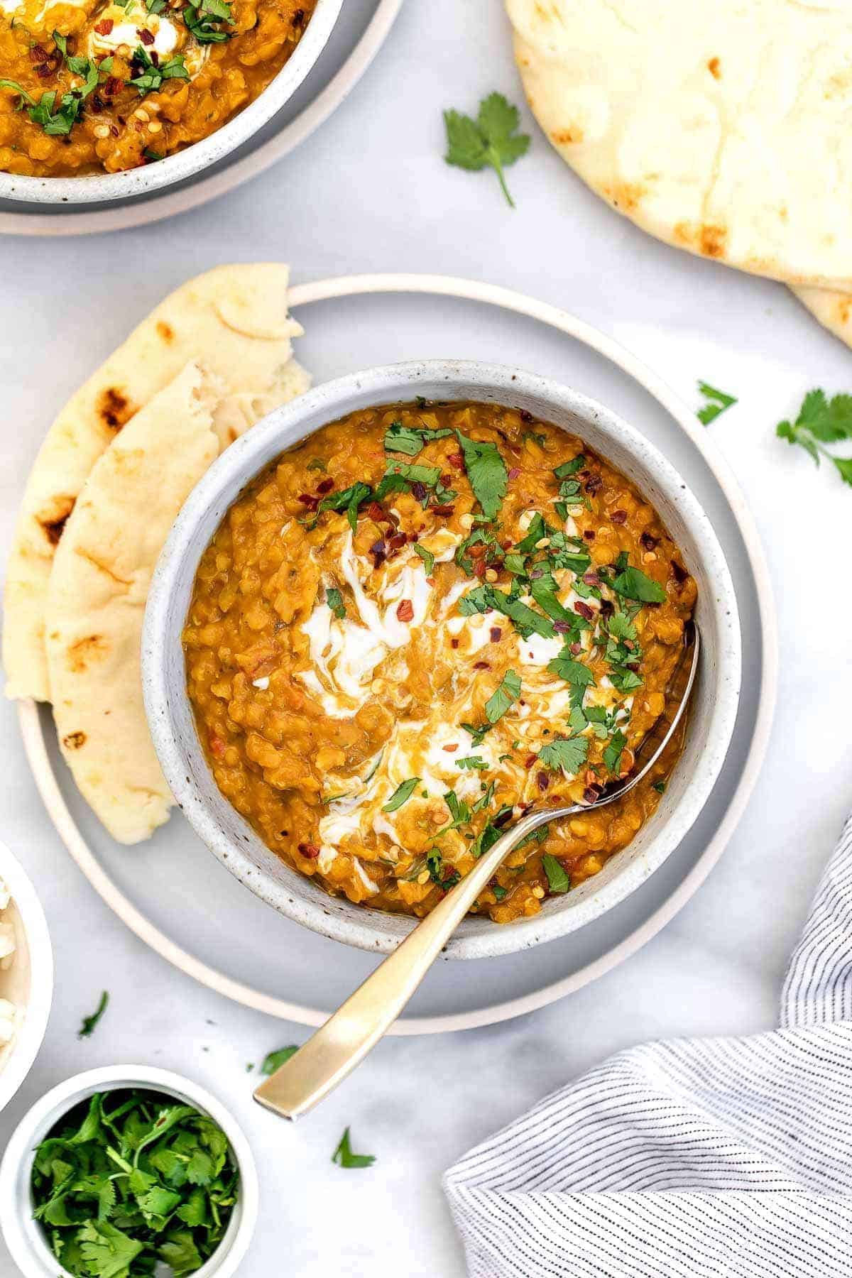 vegan Red lentil Curry in a bowl on top of a plate with naan on the side.