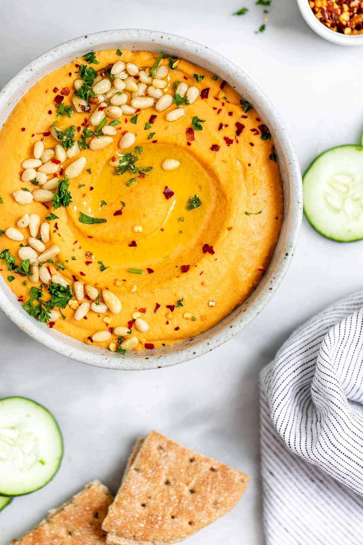 Red pepper hummus in a round bowl with pine nuts and parsley on top.