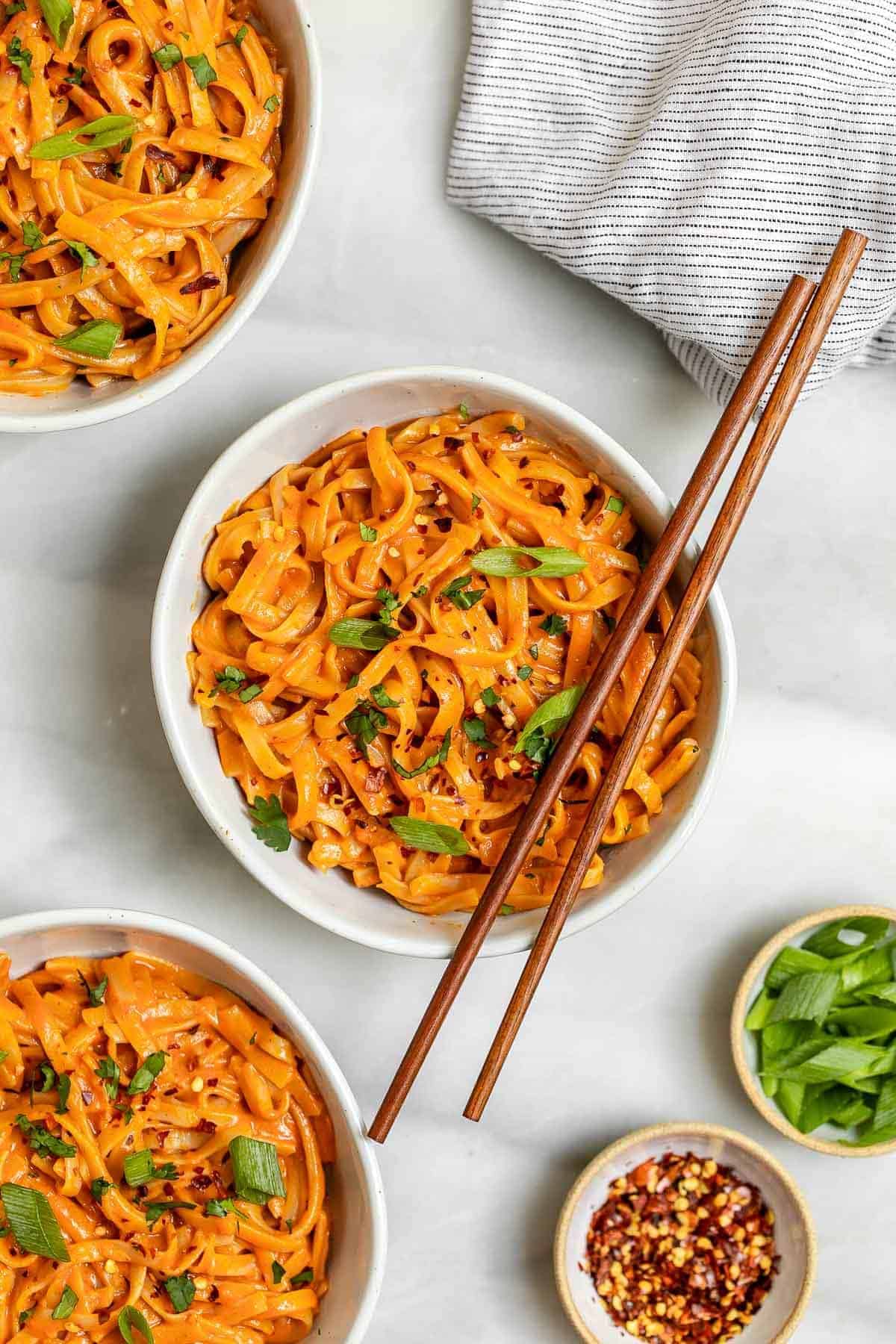 Three bowls with red curry noodles with chopsticks on top. 