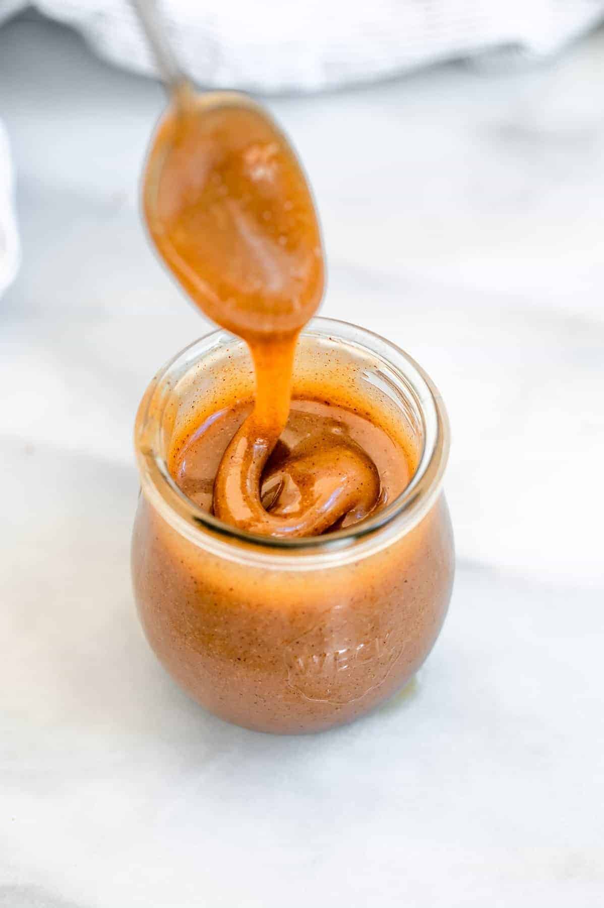 Spoon scooping out the vegan caramel from a glass jar.