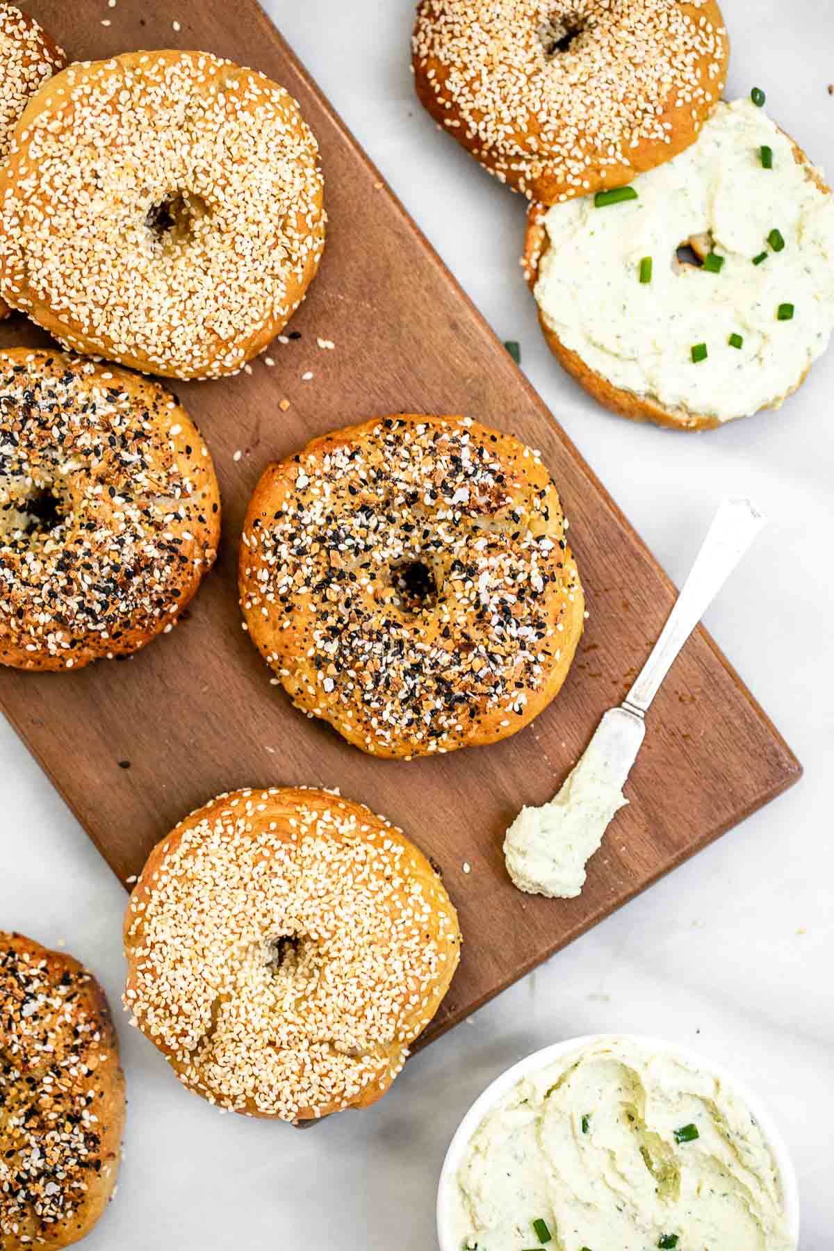 Bagels on a wooden board with a bowl of cream cheese.
