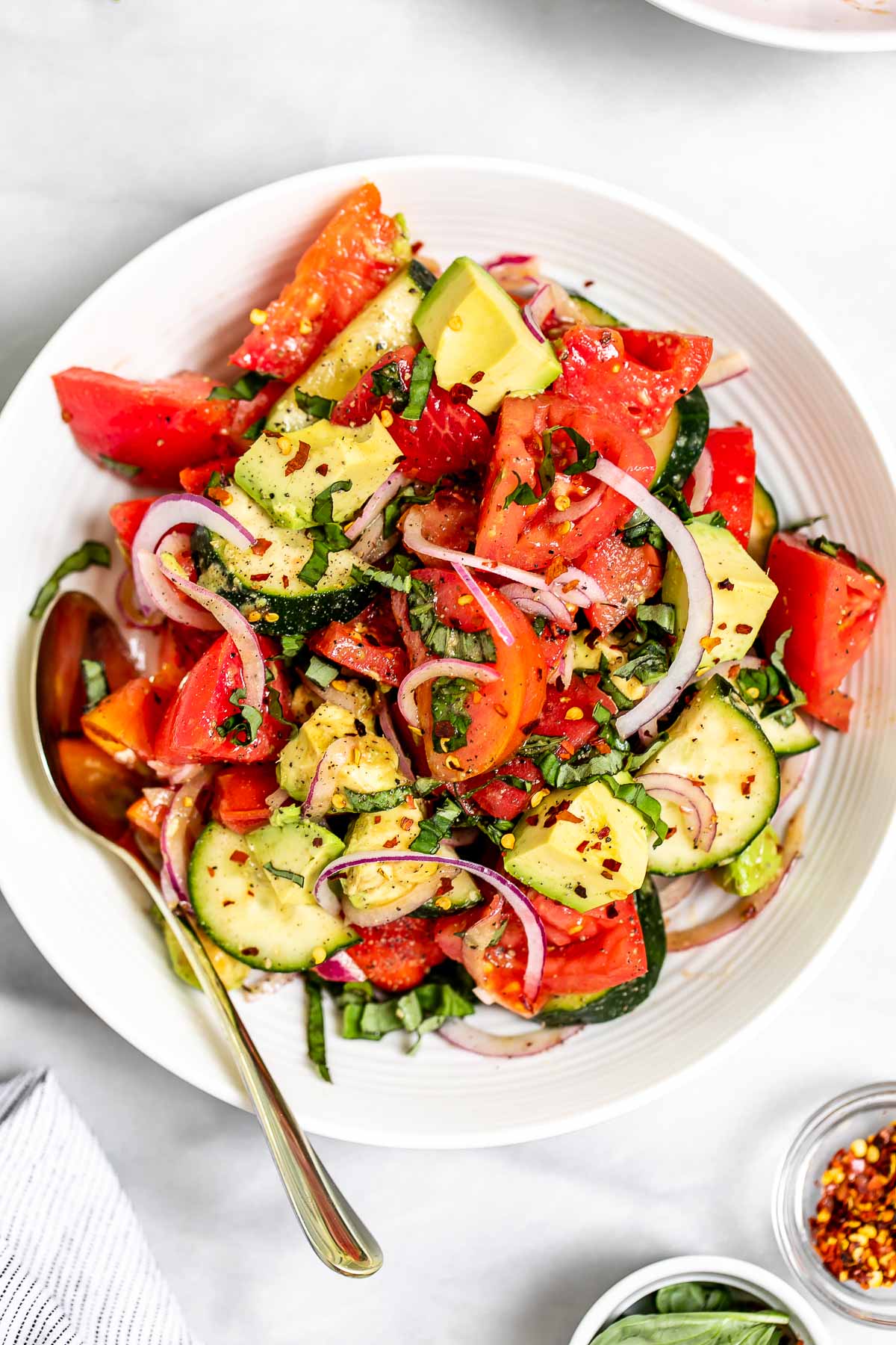 Tomato cucumber avocado salad in a bowl with fresh basil. 