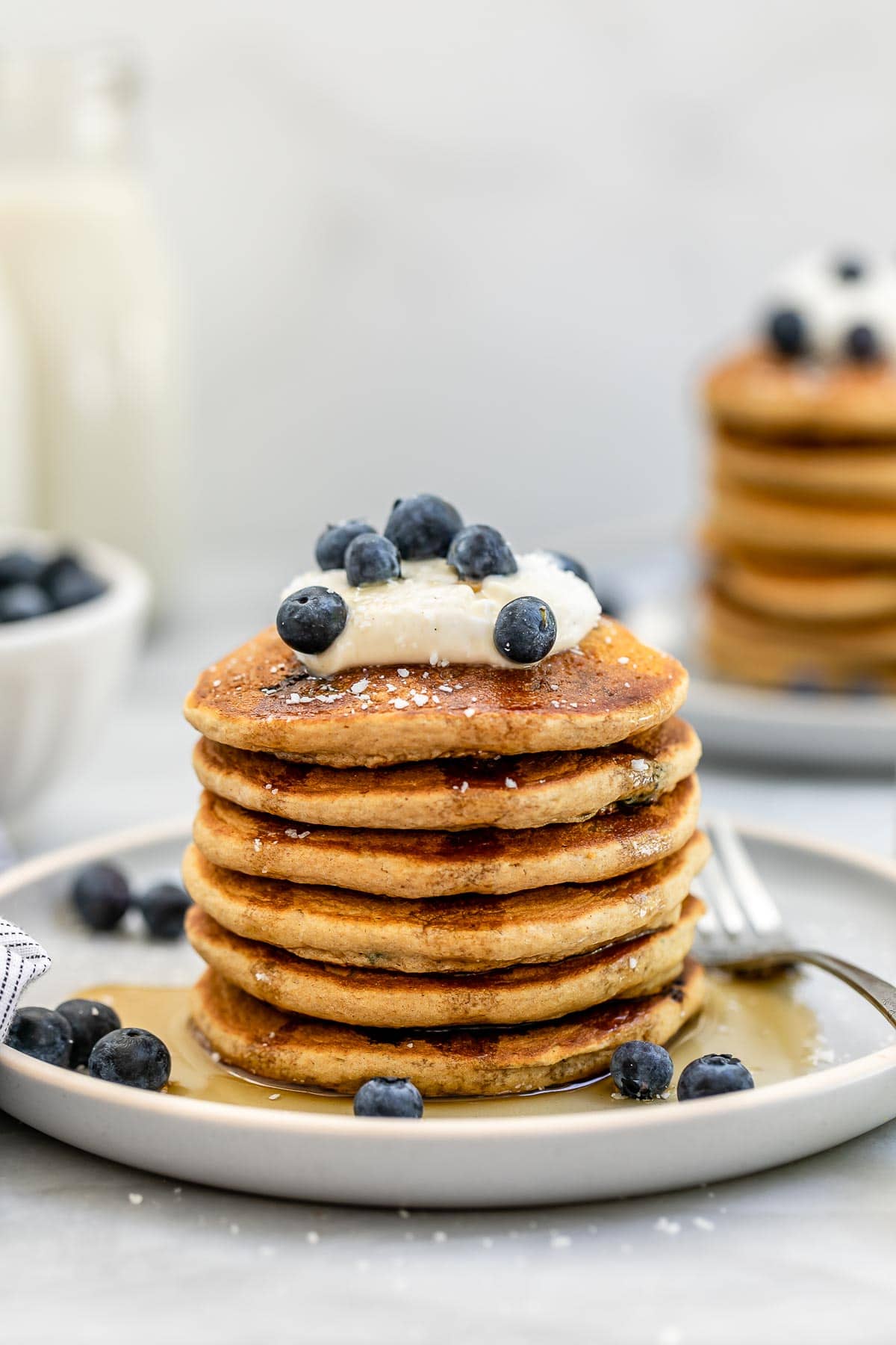 Six vegan blueberry pancakes stacked on each other with yogurt on top.