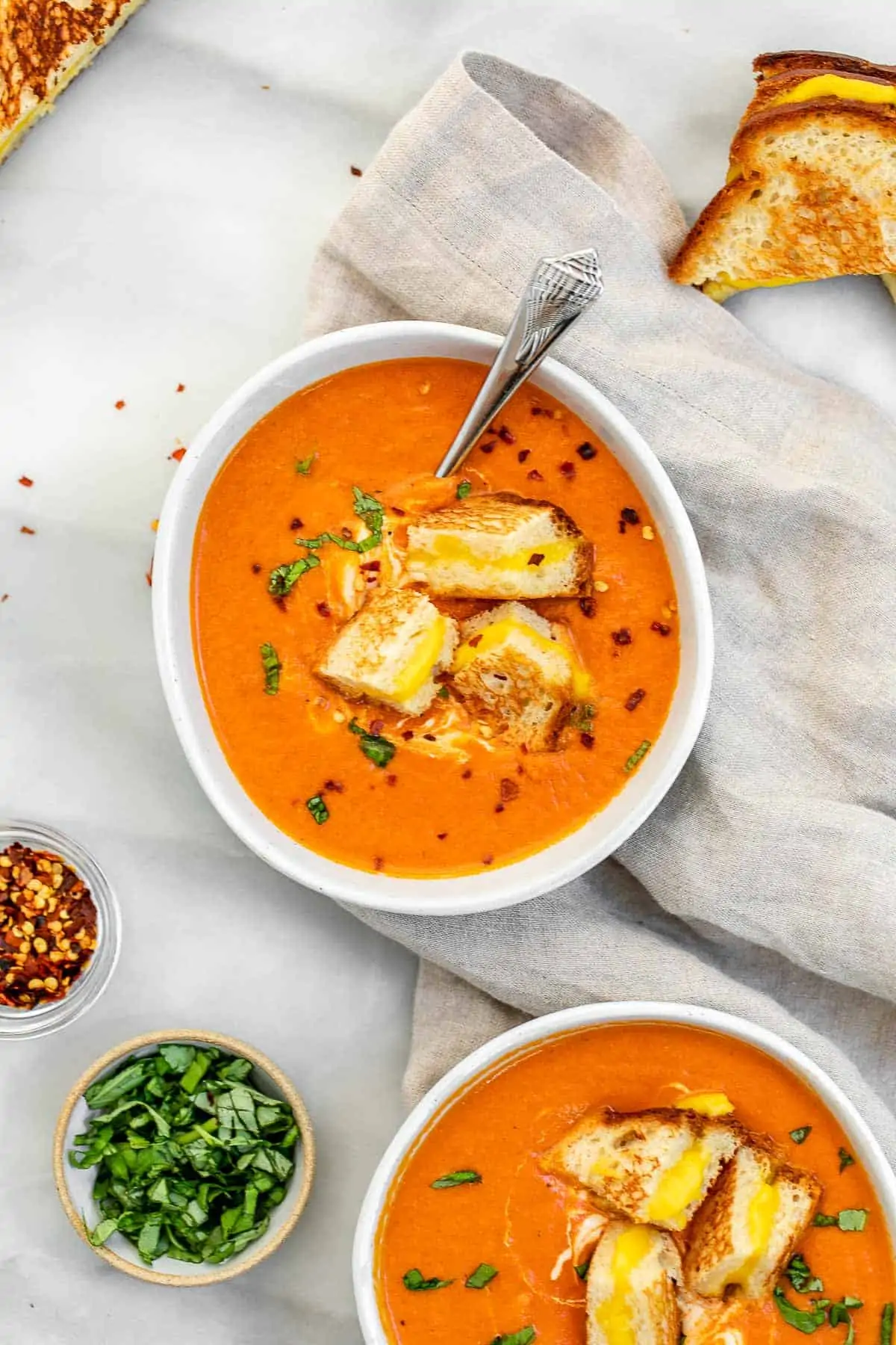 Two bowls of vegan tomato soup with grilled cheese croutons on top.