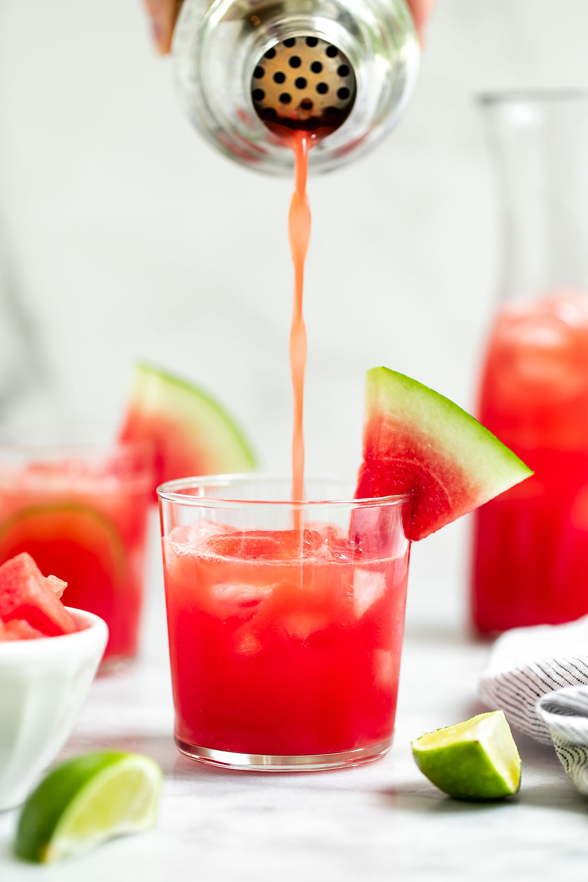 Pouring the watermelon cocktail into a glass from a cocktail shaker. 