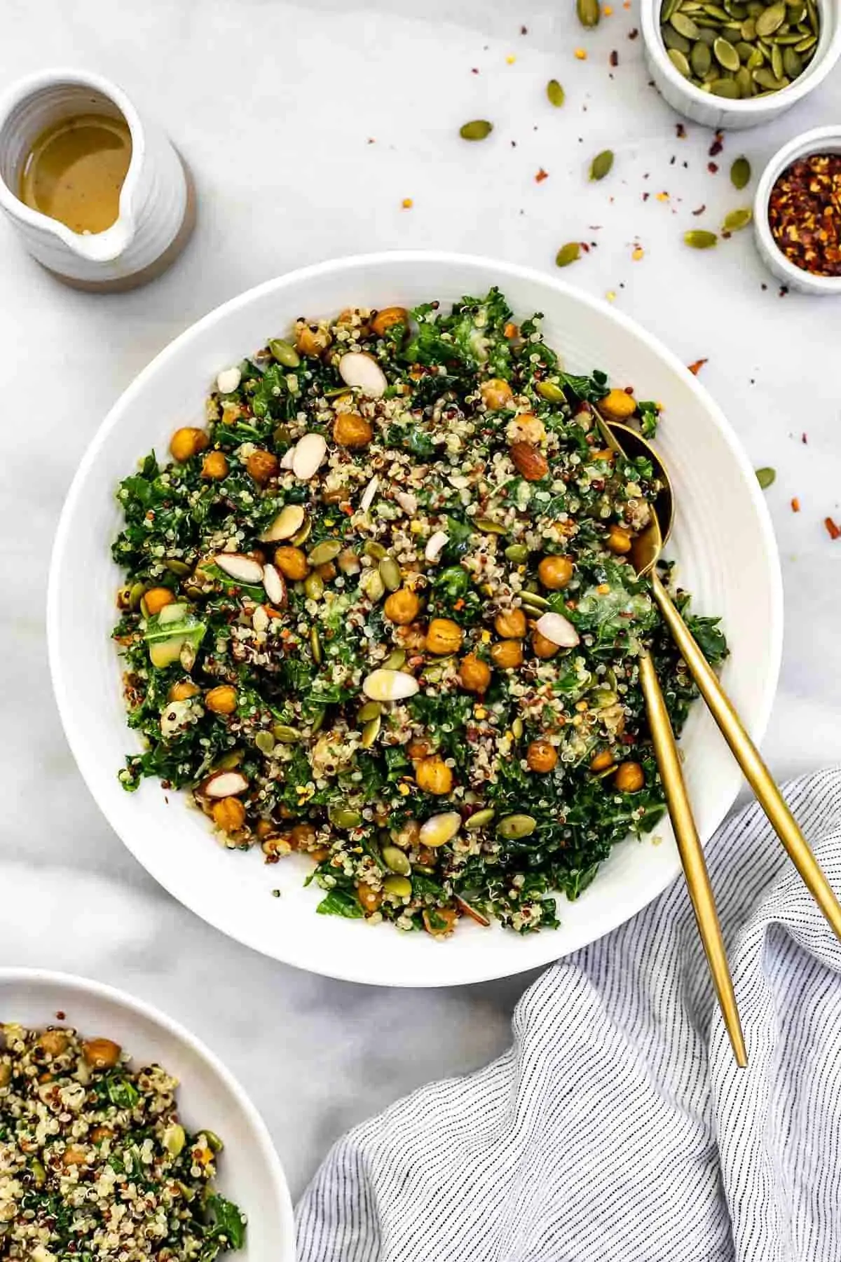 Kale quinoa salad in a white bowl with a stripped towel.