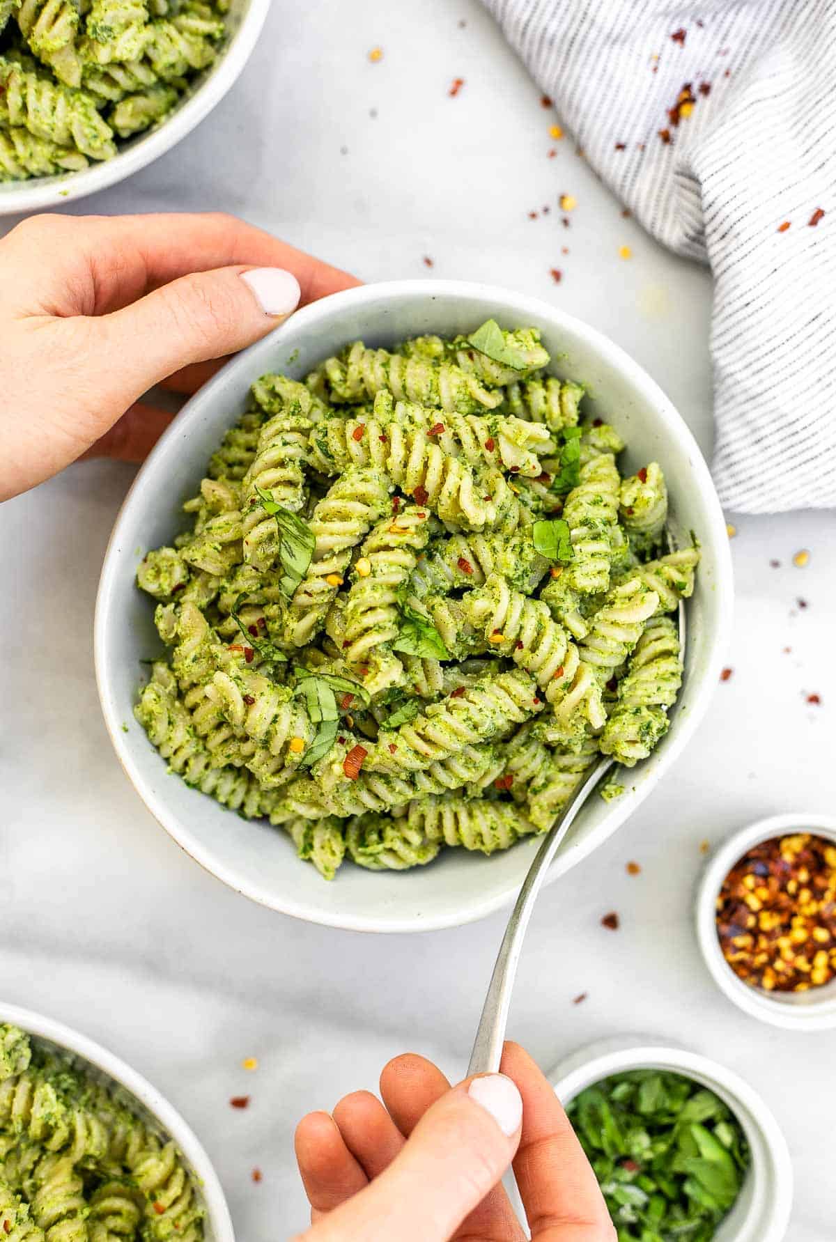 Hands holding the bowl with the nut free pesto pasta