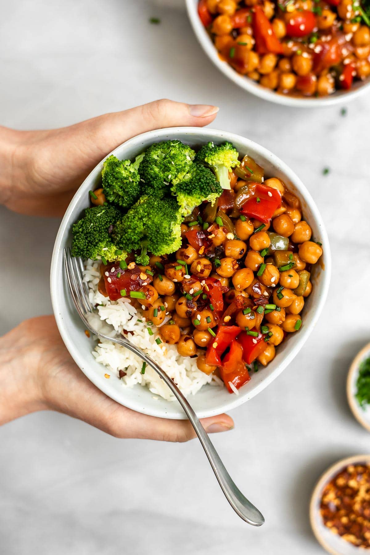 Hands holding the chickpea stir fry in a small blue bowl.