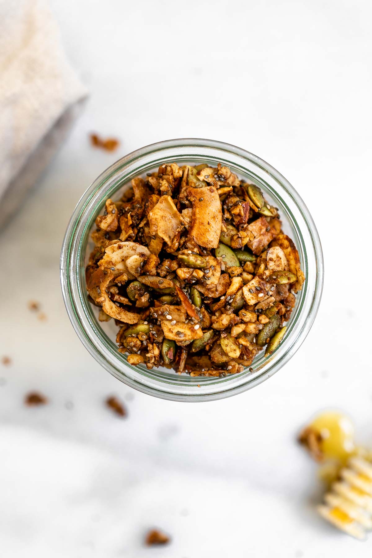 Paleo granola in a glass jar with honey on the side.