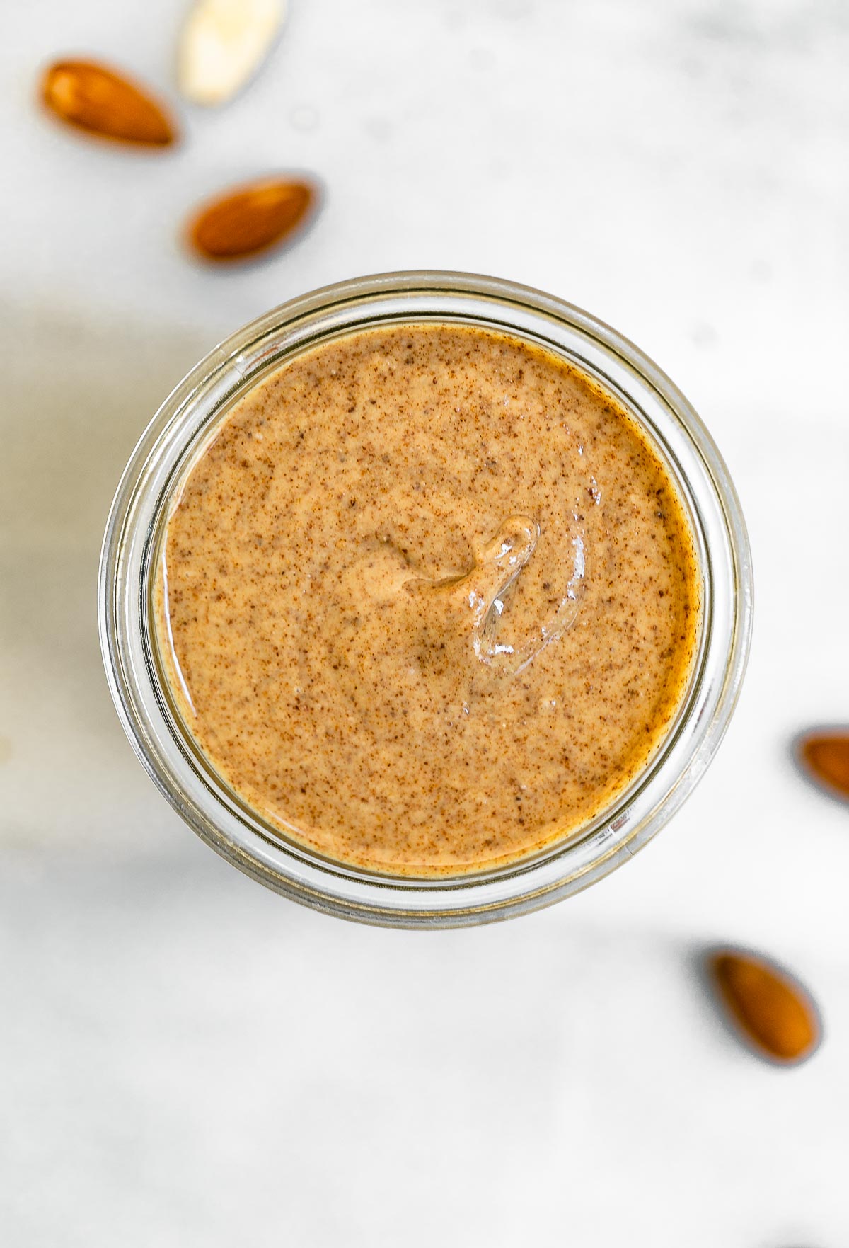 Final almond butter in a jar with almonds on the side.