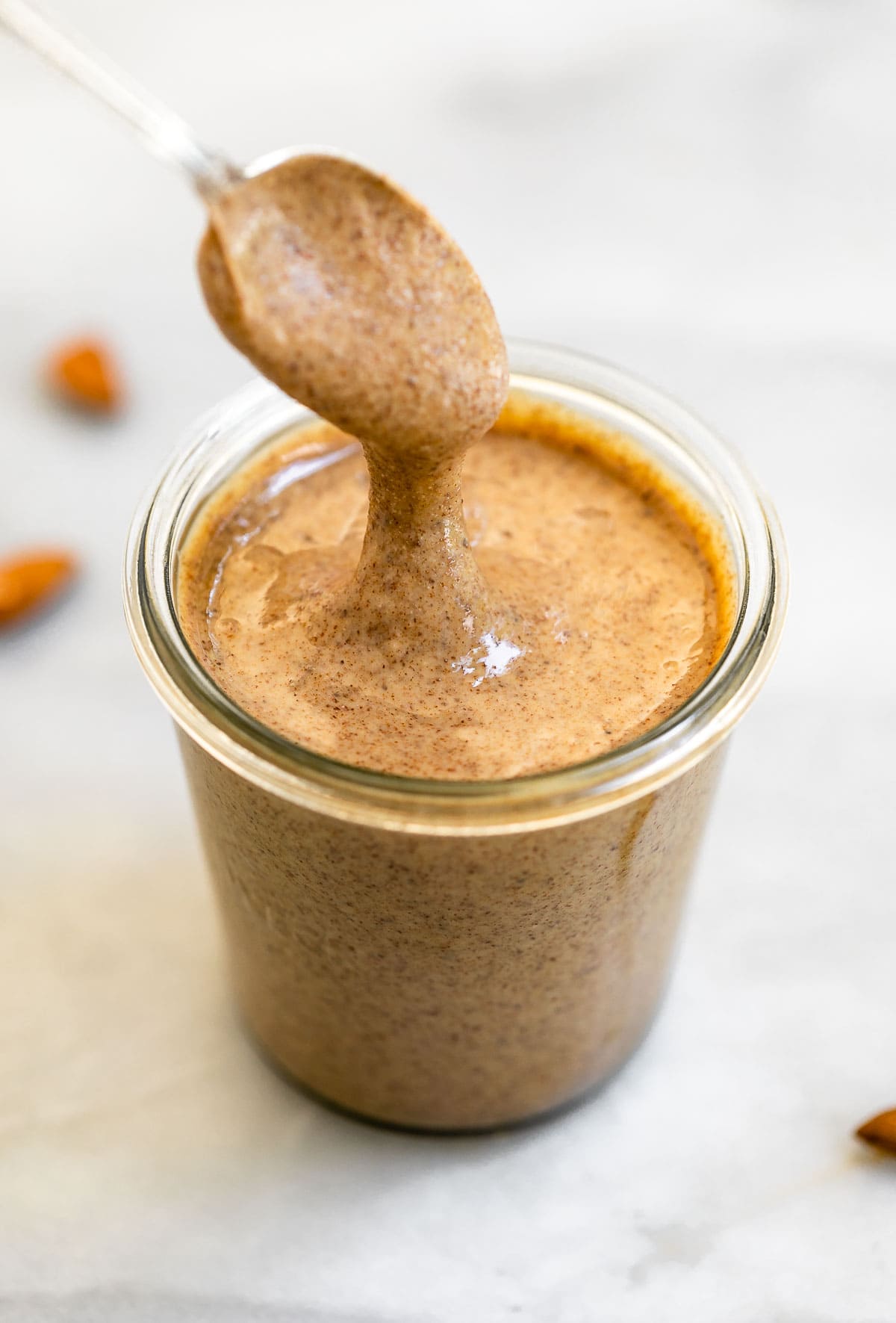 Dipping a spoon into the jar of almond butter to show the texture.