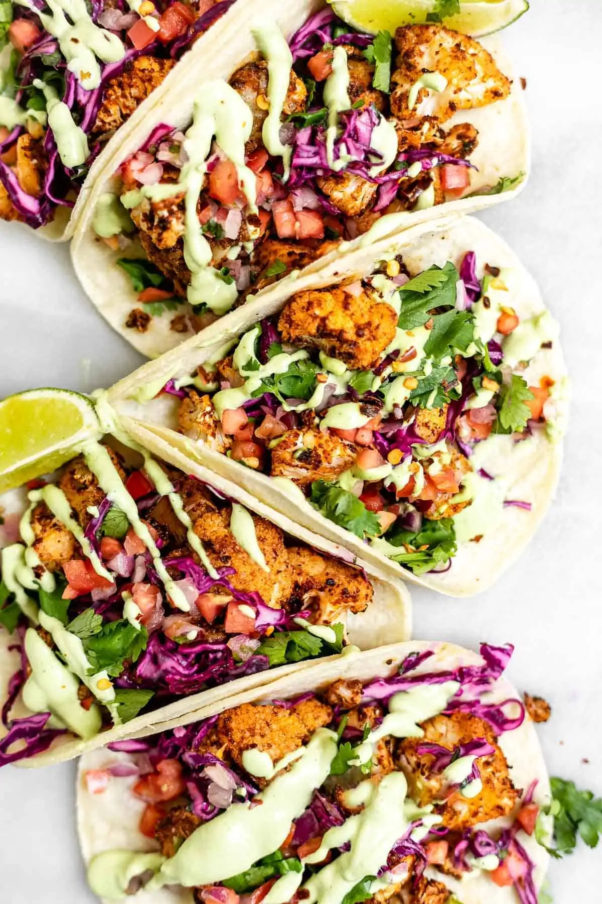 Five cauliflower tacos with lime wedges.