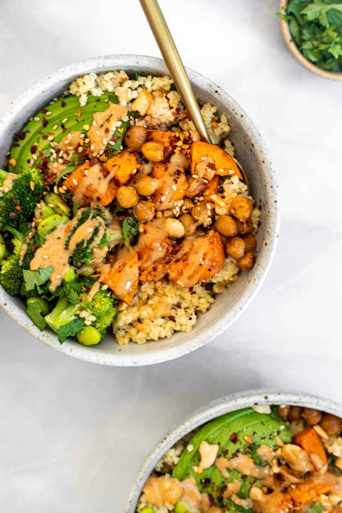 Two buddha bowls with forks on the side with millet and broccoli.