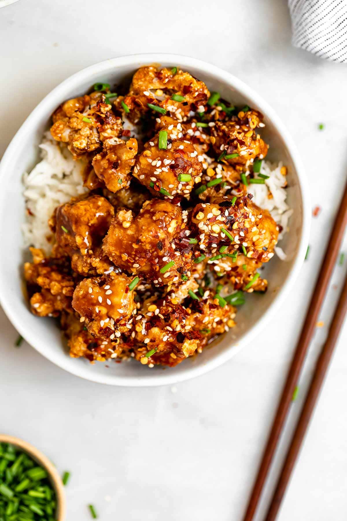 Crispy baked sesame cauliflower in a bowl with chopsticks on the side.