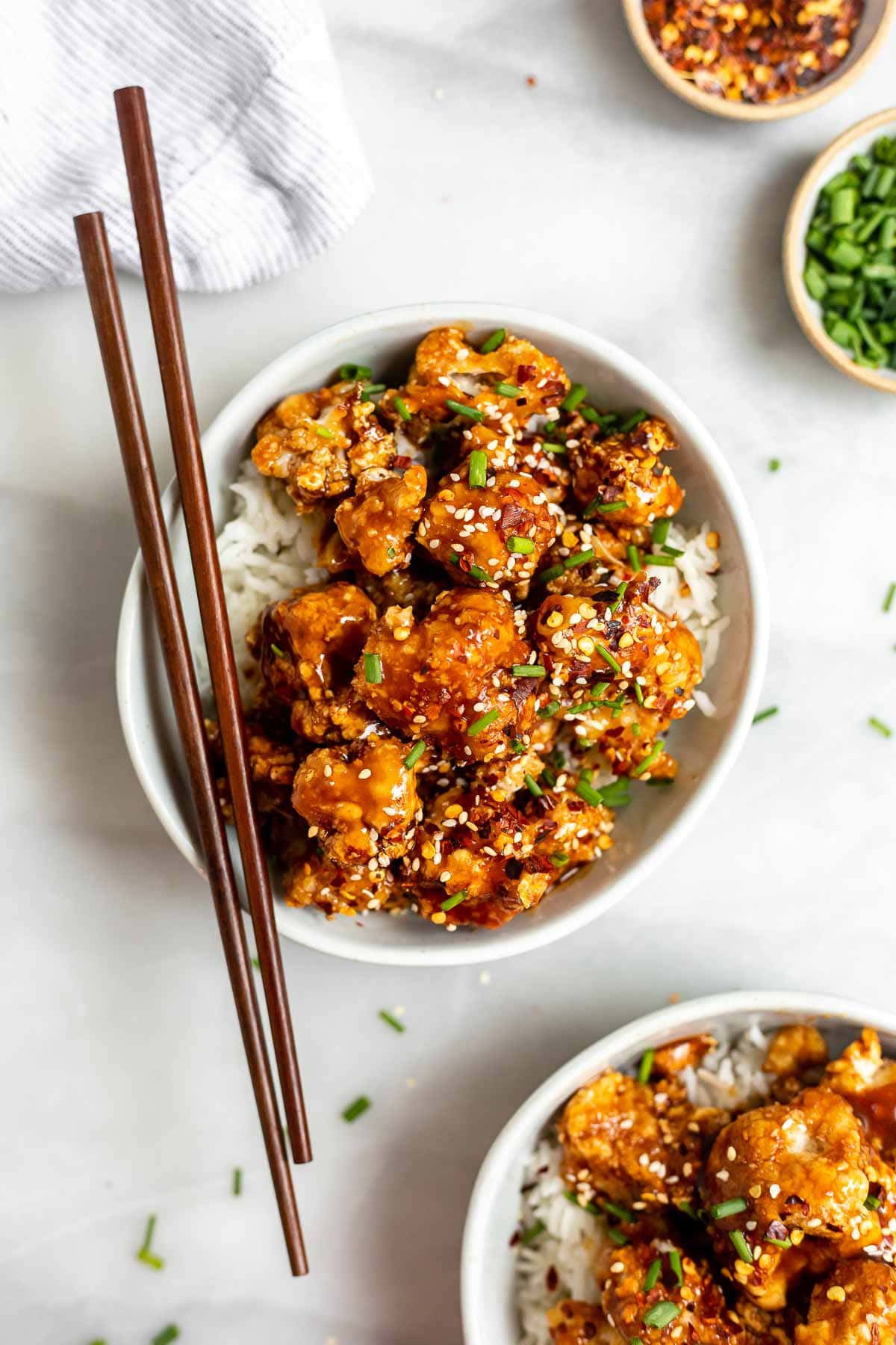 Vegan crispy sesame cauliflower in a bowl with rice and chopsticks.