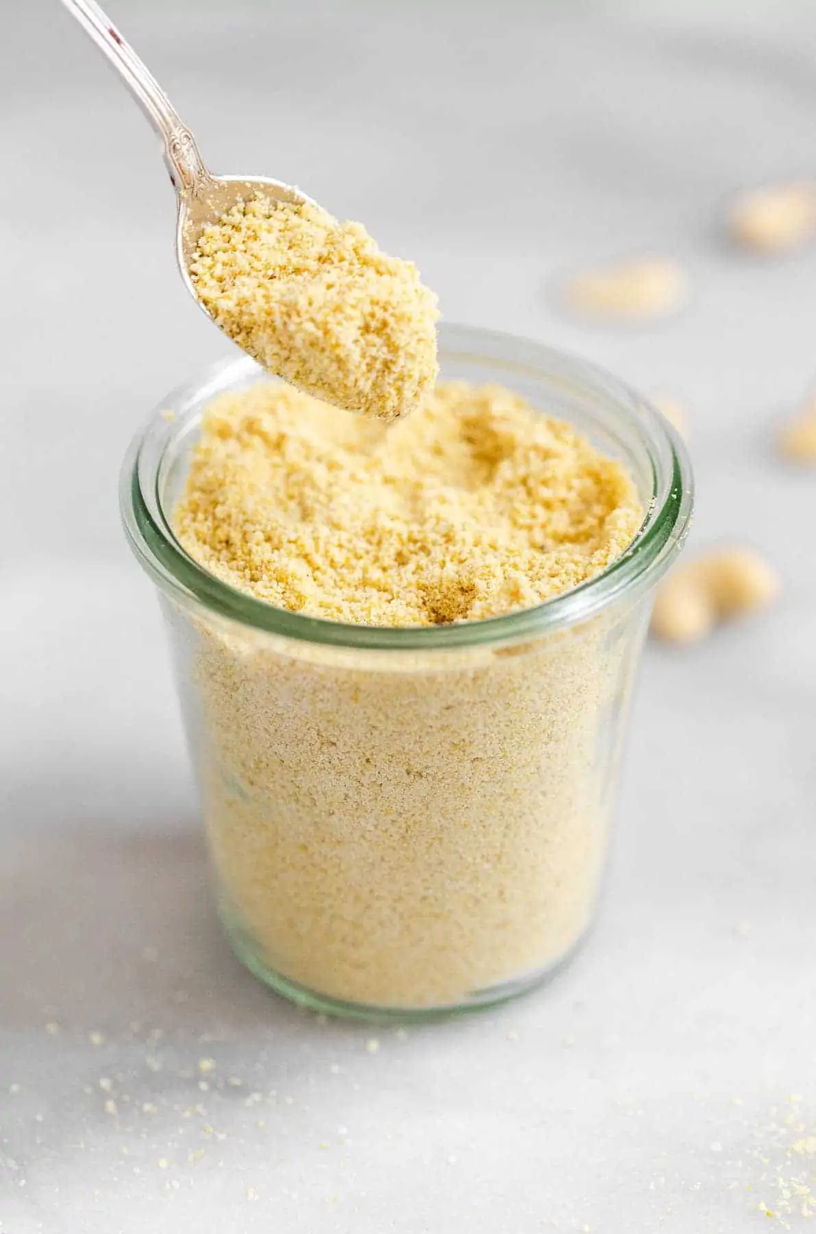 Cashew parmesan in a glass container with a spoon sprinkling it.