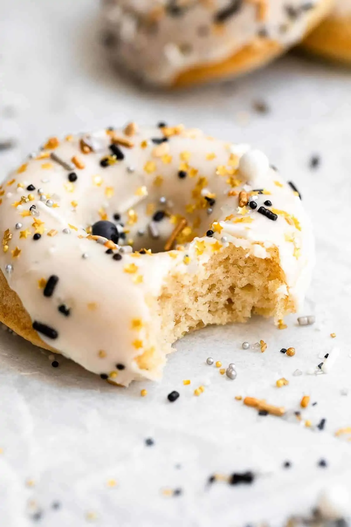 One champagne donut with a bite taken out with sprinkles on top.