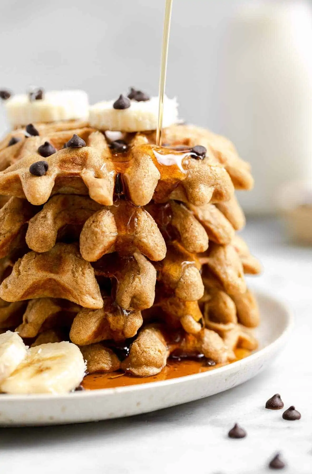 Fives waffles stacked on each other with banana and maple syrup.