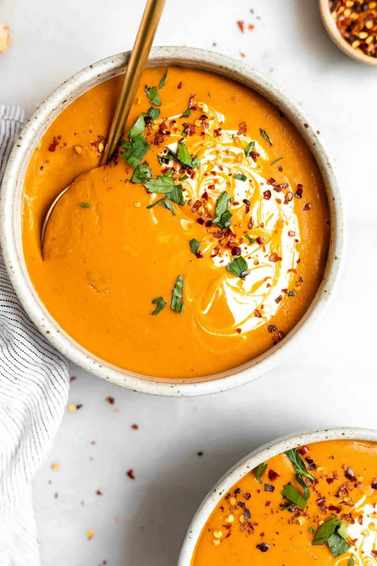 Red lentil and carrot soup with chopped parsley in a white bowl.