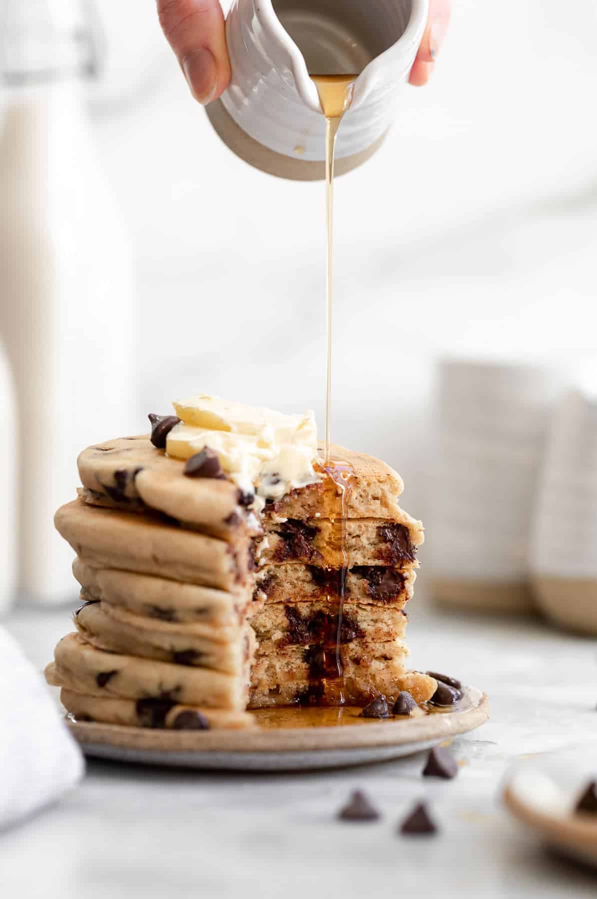 pouring maple syrup on top of the pancakes with a bite taken out
