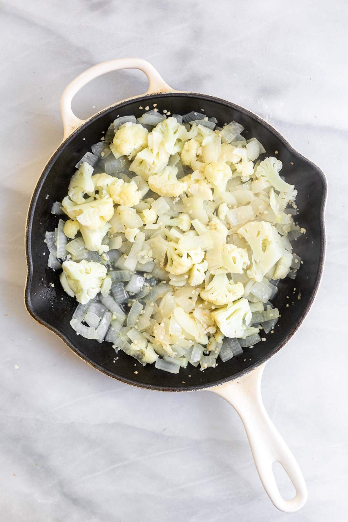 Onion and cauliflower sauteing in a pan.