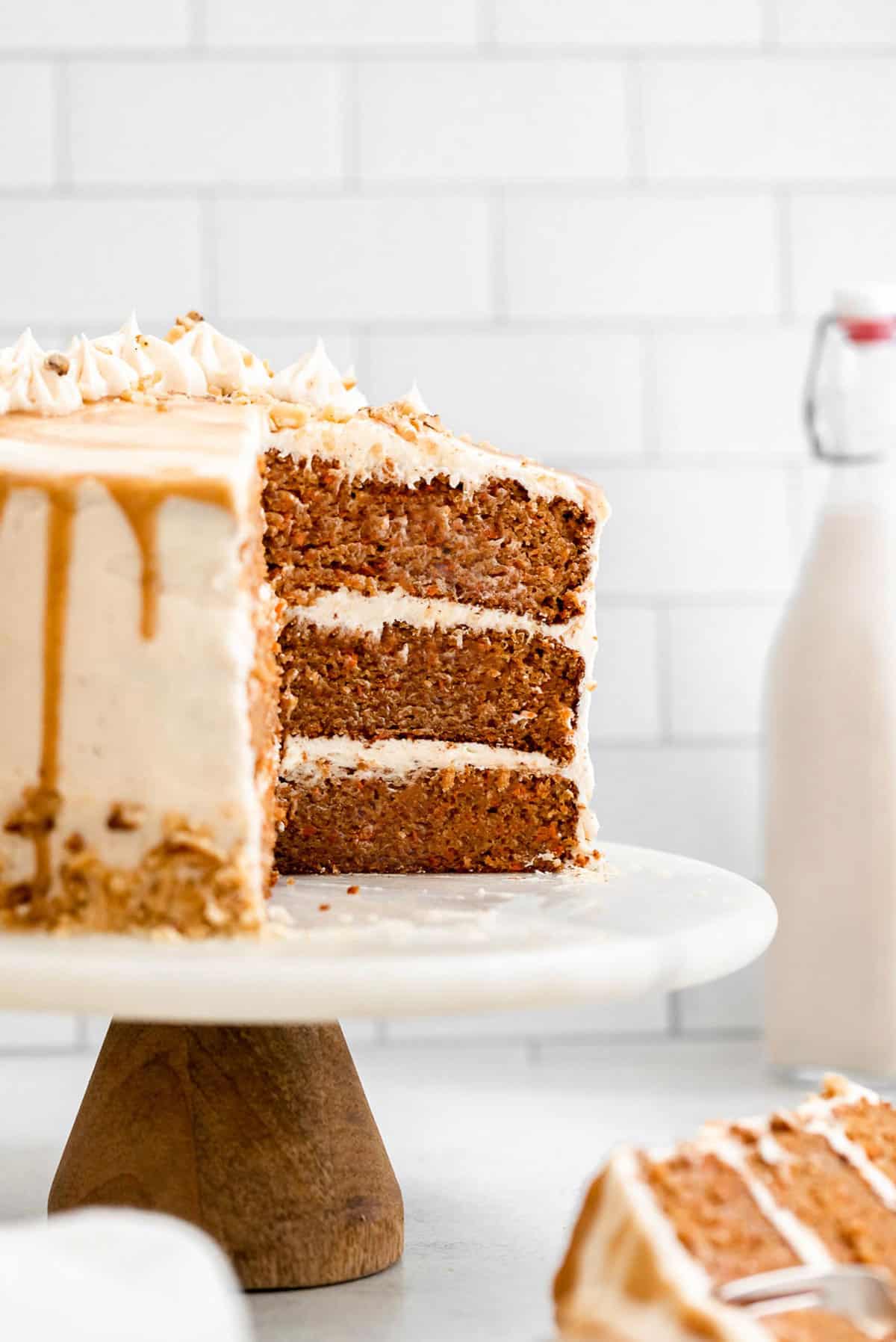 three layer gluten free carrot cake on a cake stand with milk in the back