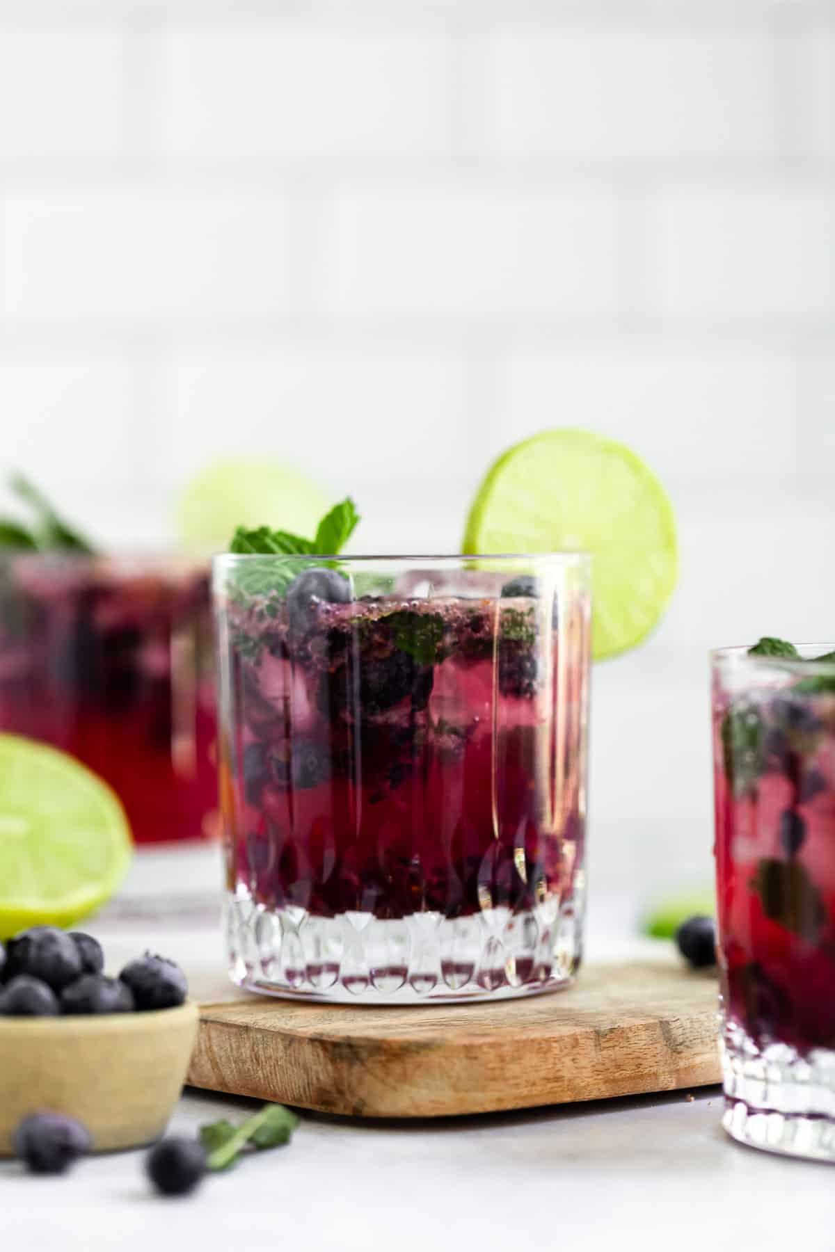 three glasses with blueberry mojito and lime wedges