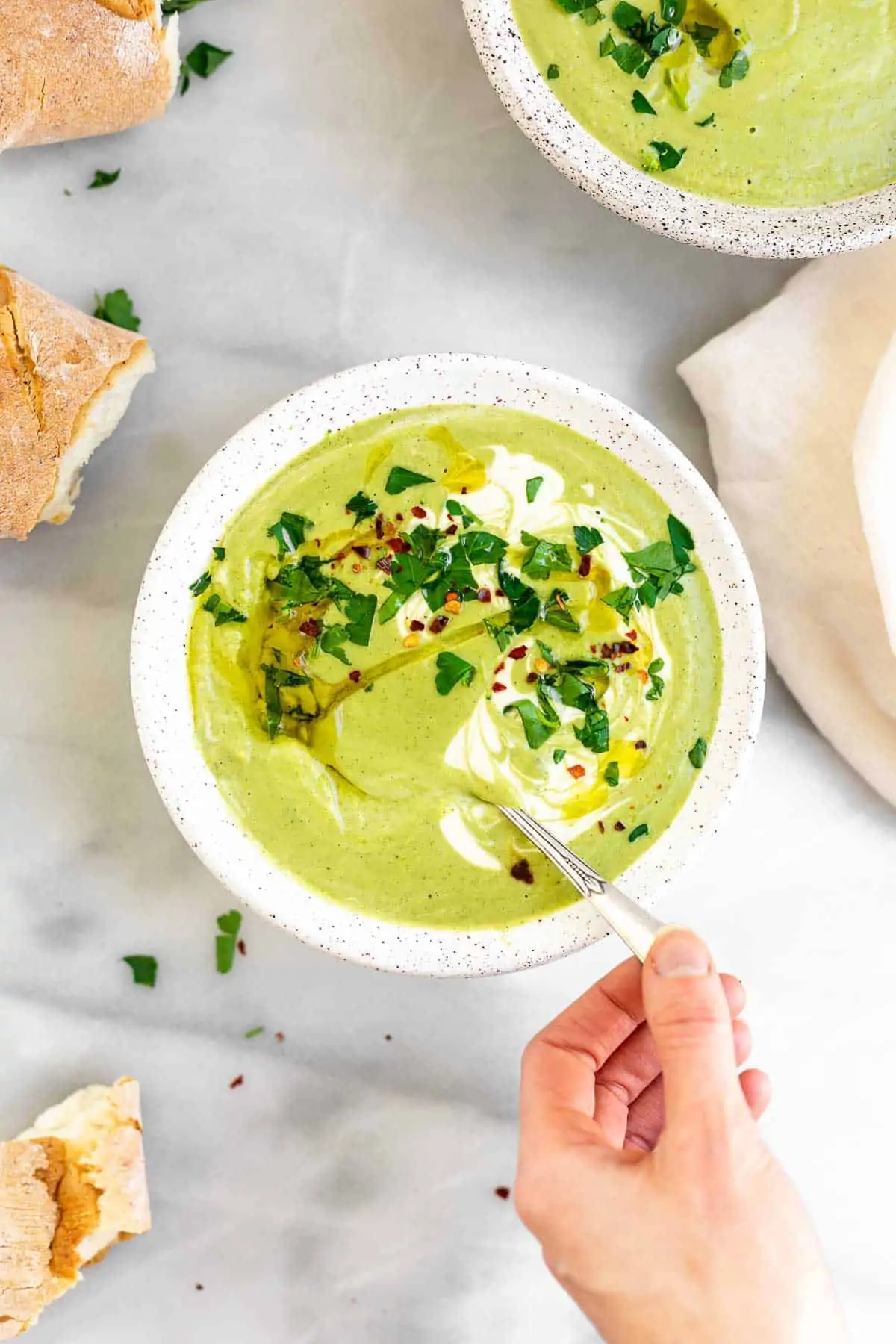 hand holding a spoon with the cream of broccoli soup with parsley