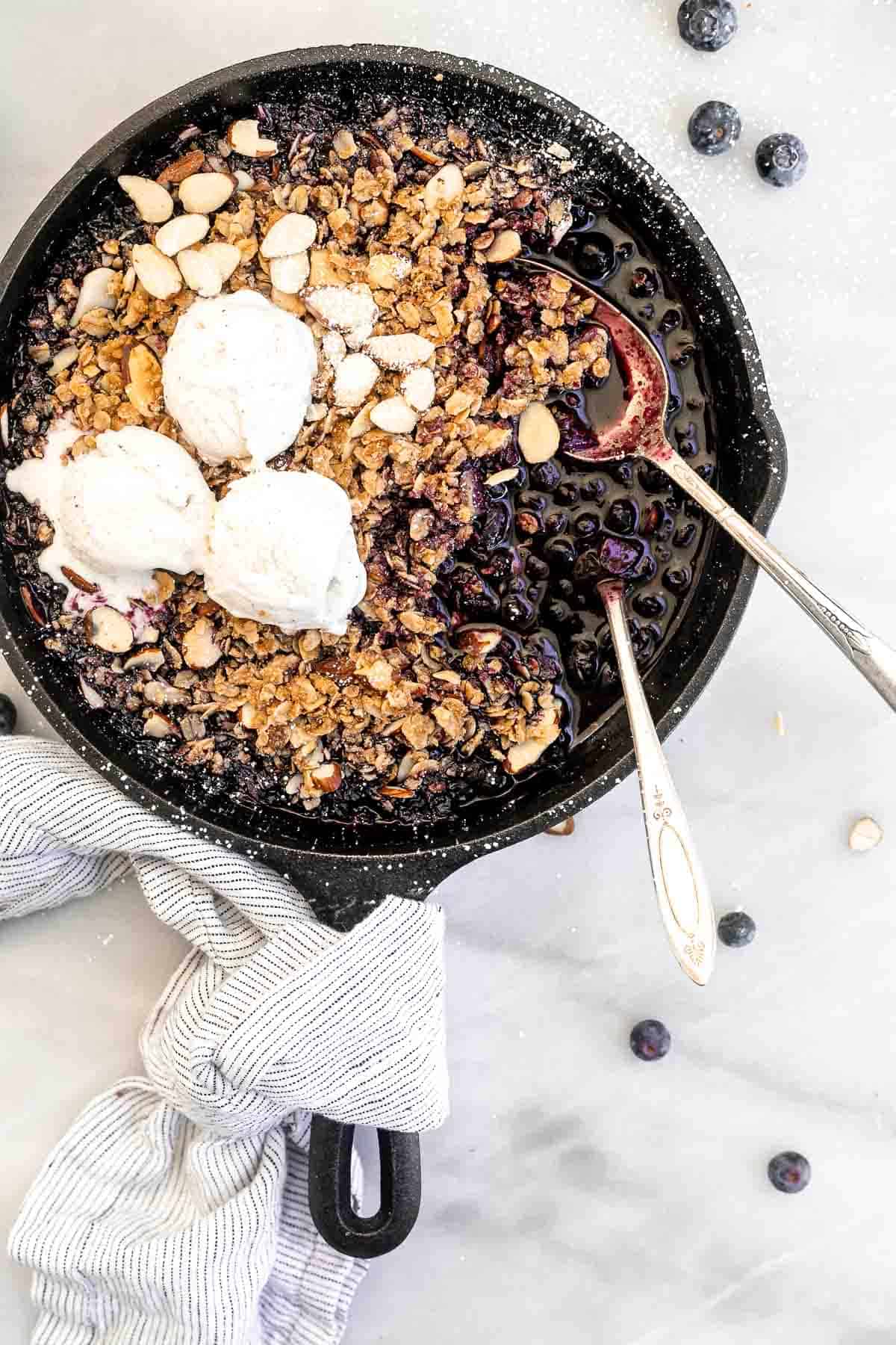 gluten free blueberry crisp in a cast iron skillet with ice cream