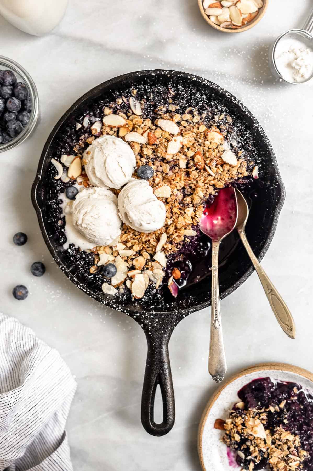 blueberry crisp in a cast iron pan with two spoons on the side
