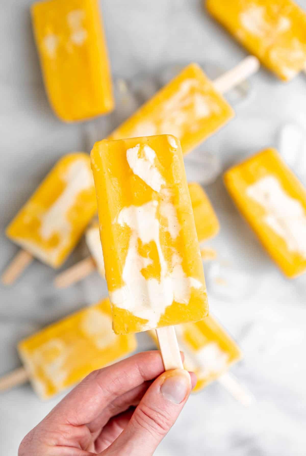 holding a pineapple mango popsicle by the stick