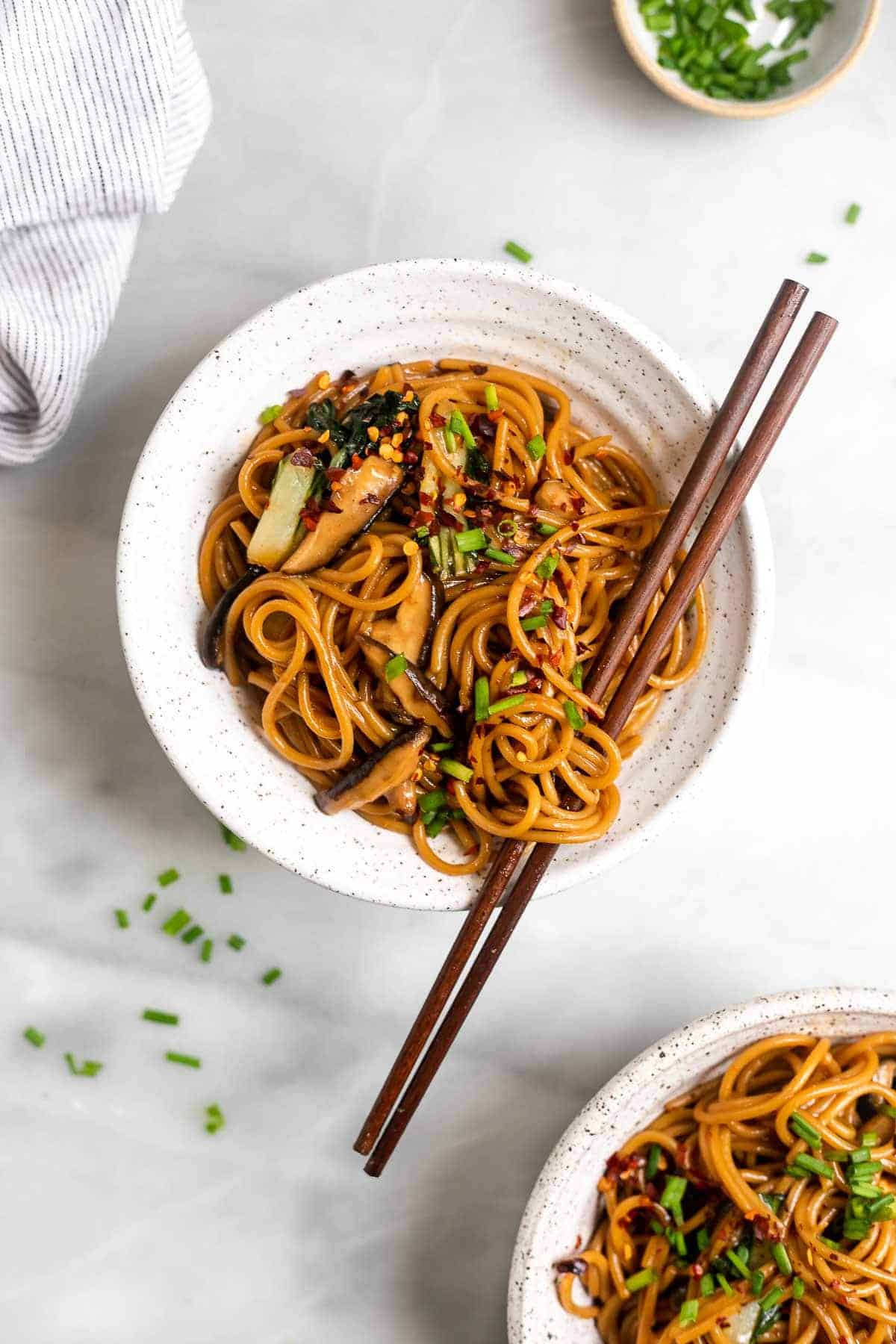 two bowls of stir fry noodles with chopsticks and mushrooms