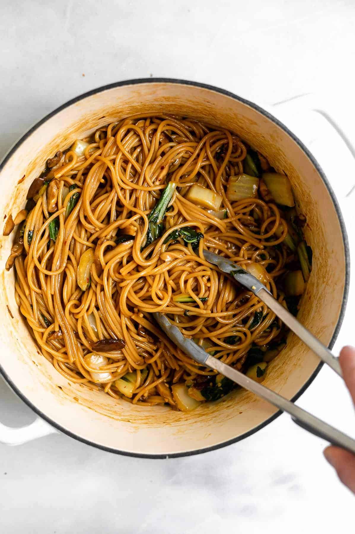 vegan teriyaki noodles in a large white pot with tongs